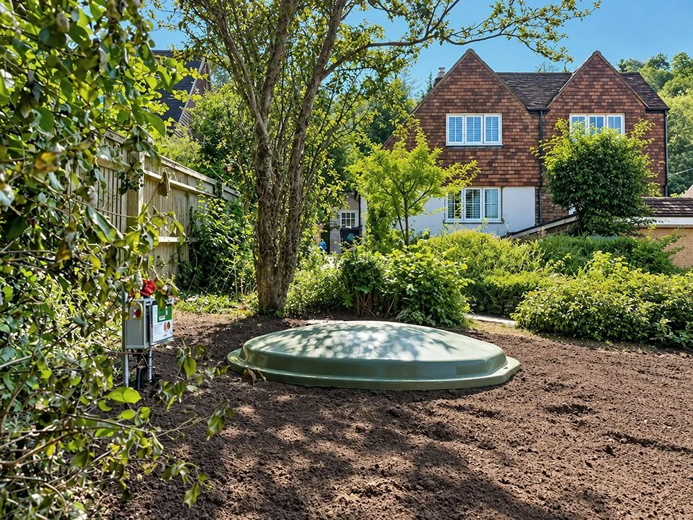 Installed drainage tank with a green access cover beside a house.