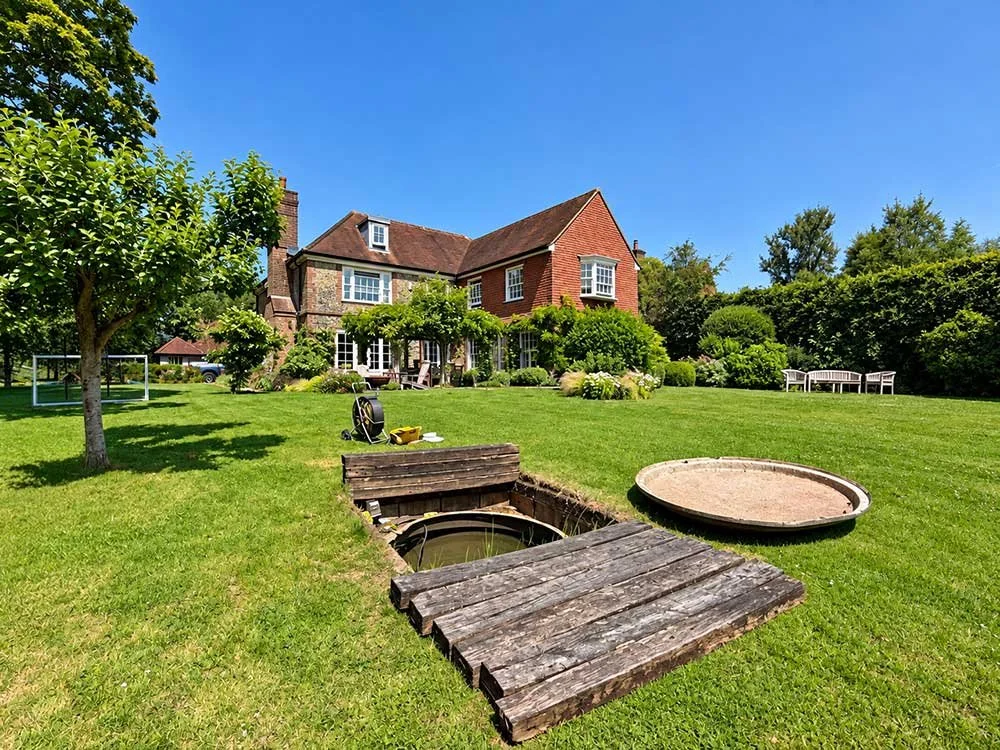 Open drainage access chamber in the garden of a detached house.