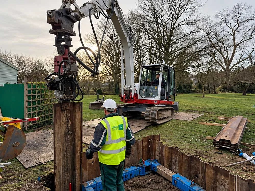 WES worker beside a supported excavation during drainage installation.