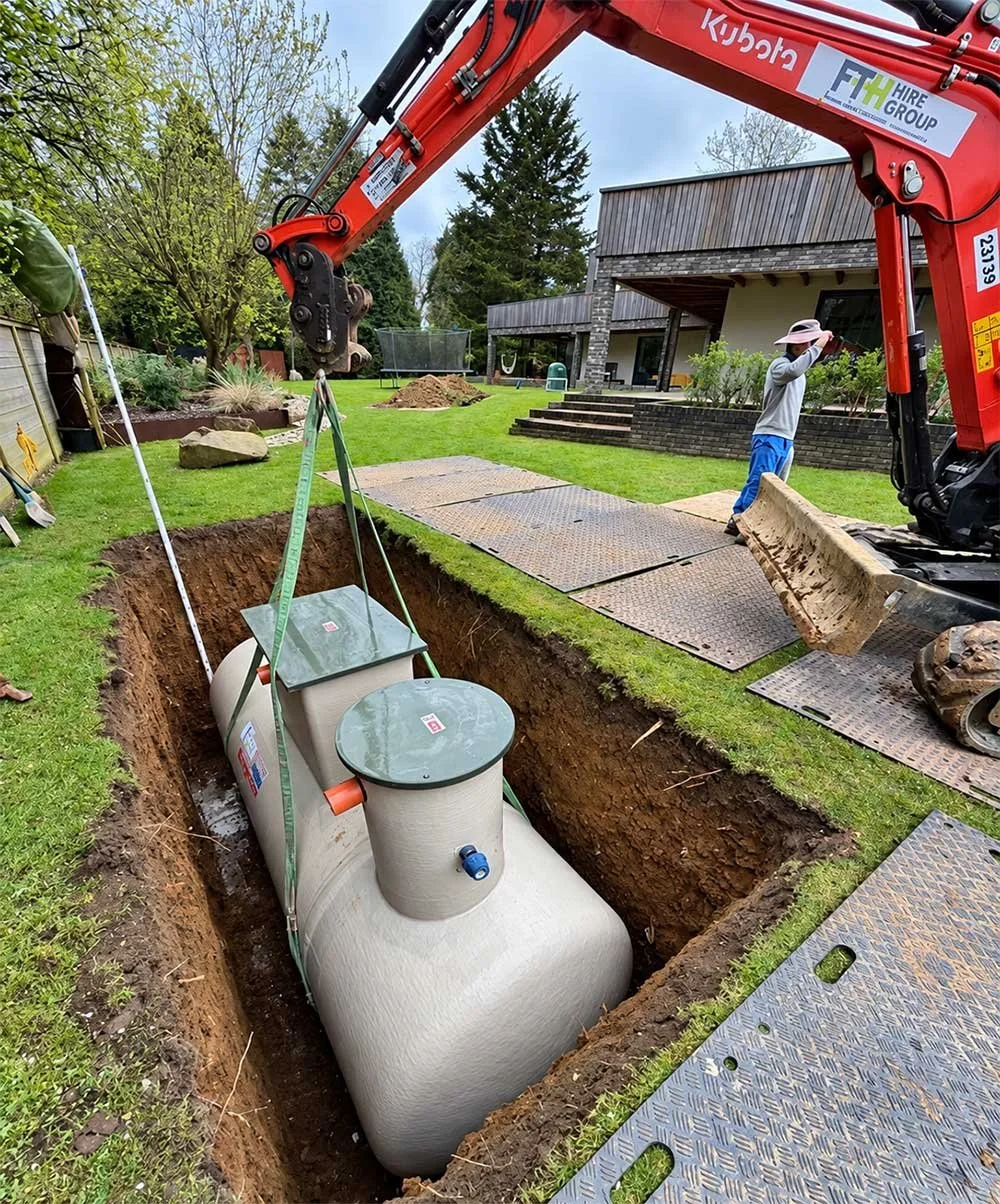 Drainage tank being lowered into a garden excavation.