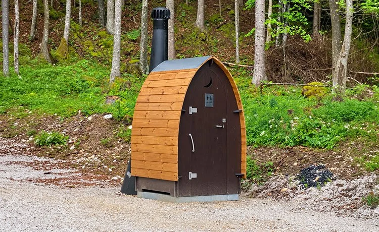 Timber toilet cabin with a pointed roof and ventilation chimney.