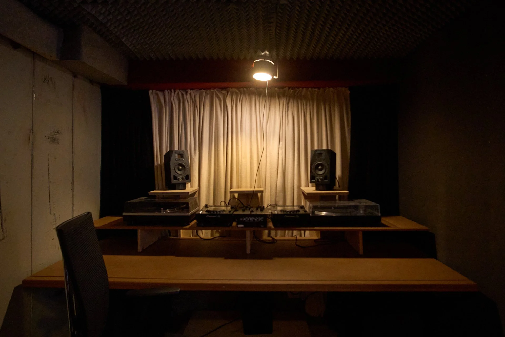 Musikstudio mit DJ-Equipment, Lautsprechern, einer Tisch-Phono und einem Vorhang im Hintergrund, in einem dunklen Raum mit beleuchteter Decke.