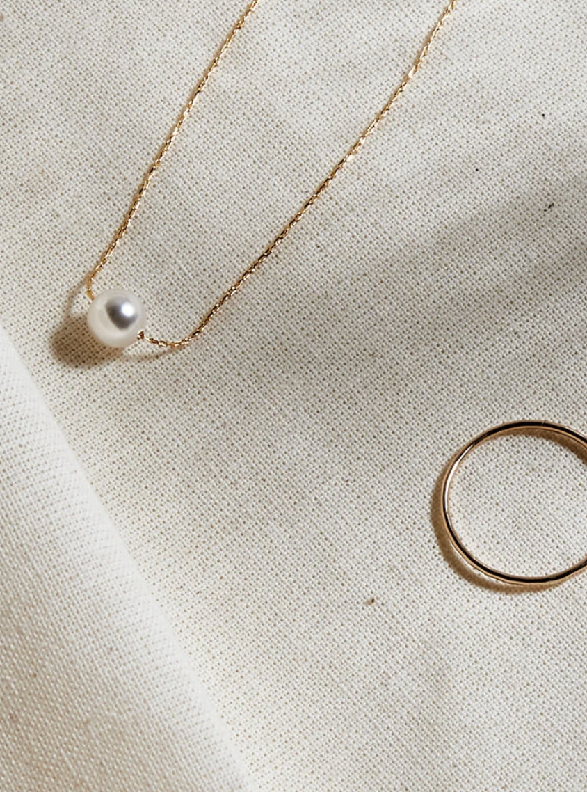 A necklace with a pearl pendant, a gold ring, and a gold bracelet on beige fabric.