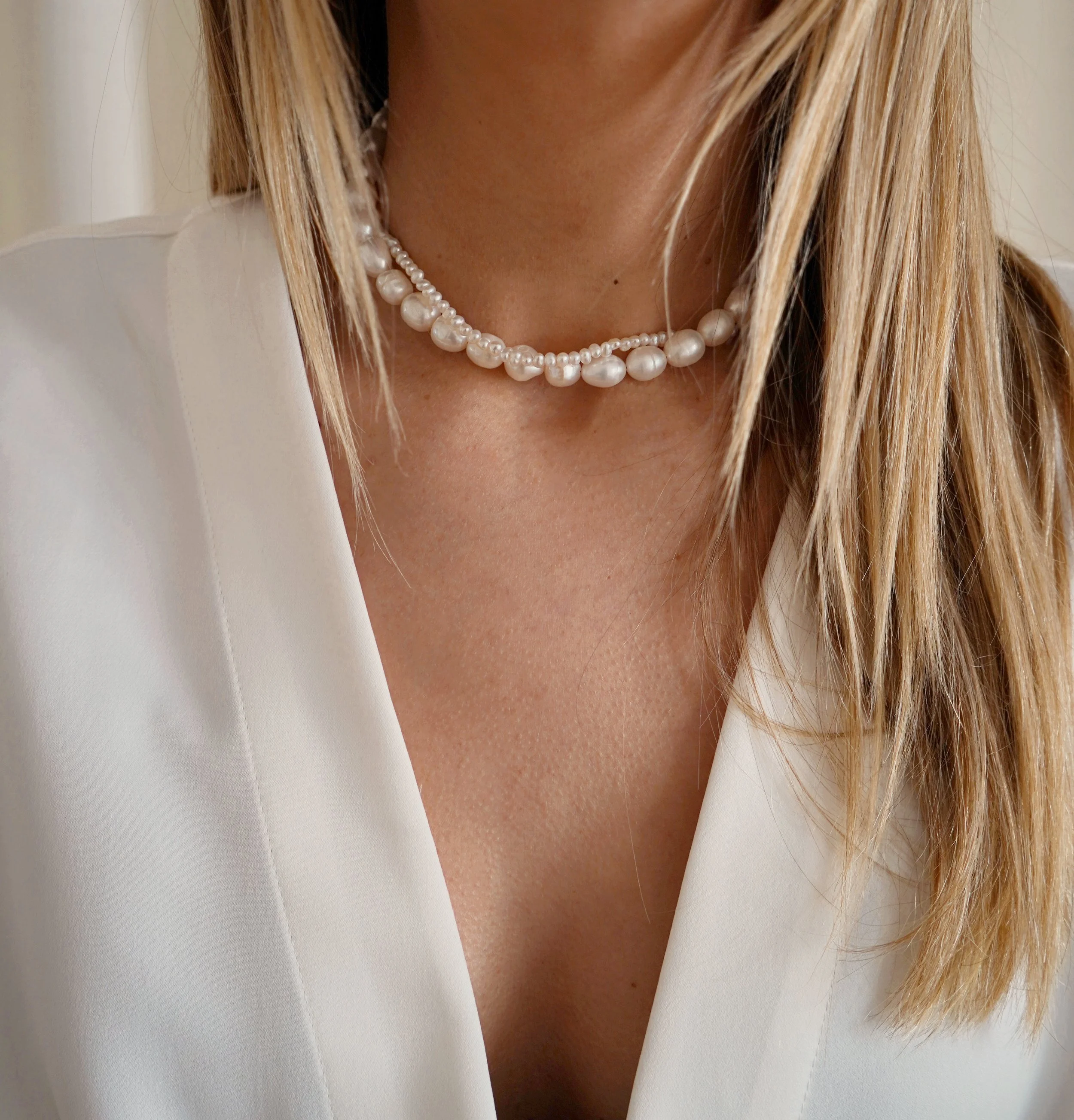 Gorge haute d'une femme portant un collier de perles blanches et une robe blanche.