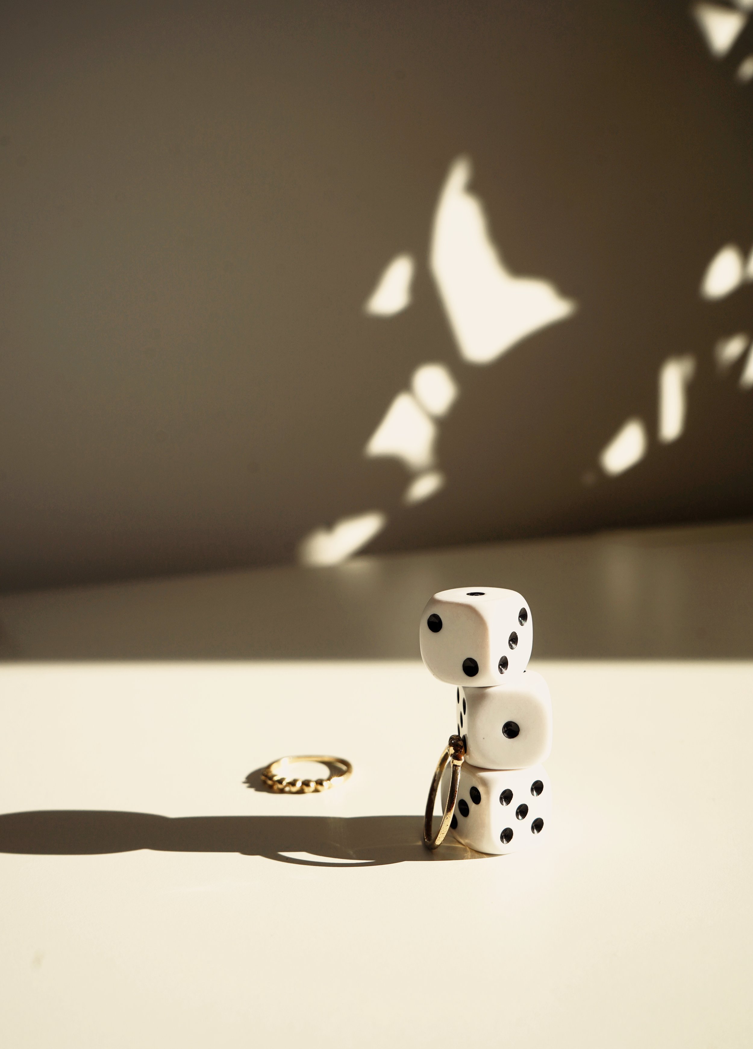 Un dé à six faces blanc avec des points noirs, un anneau en or, et un porte-clés en forme de dé, tous posés sur une surface claire avec des ombres portées.