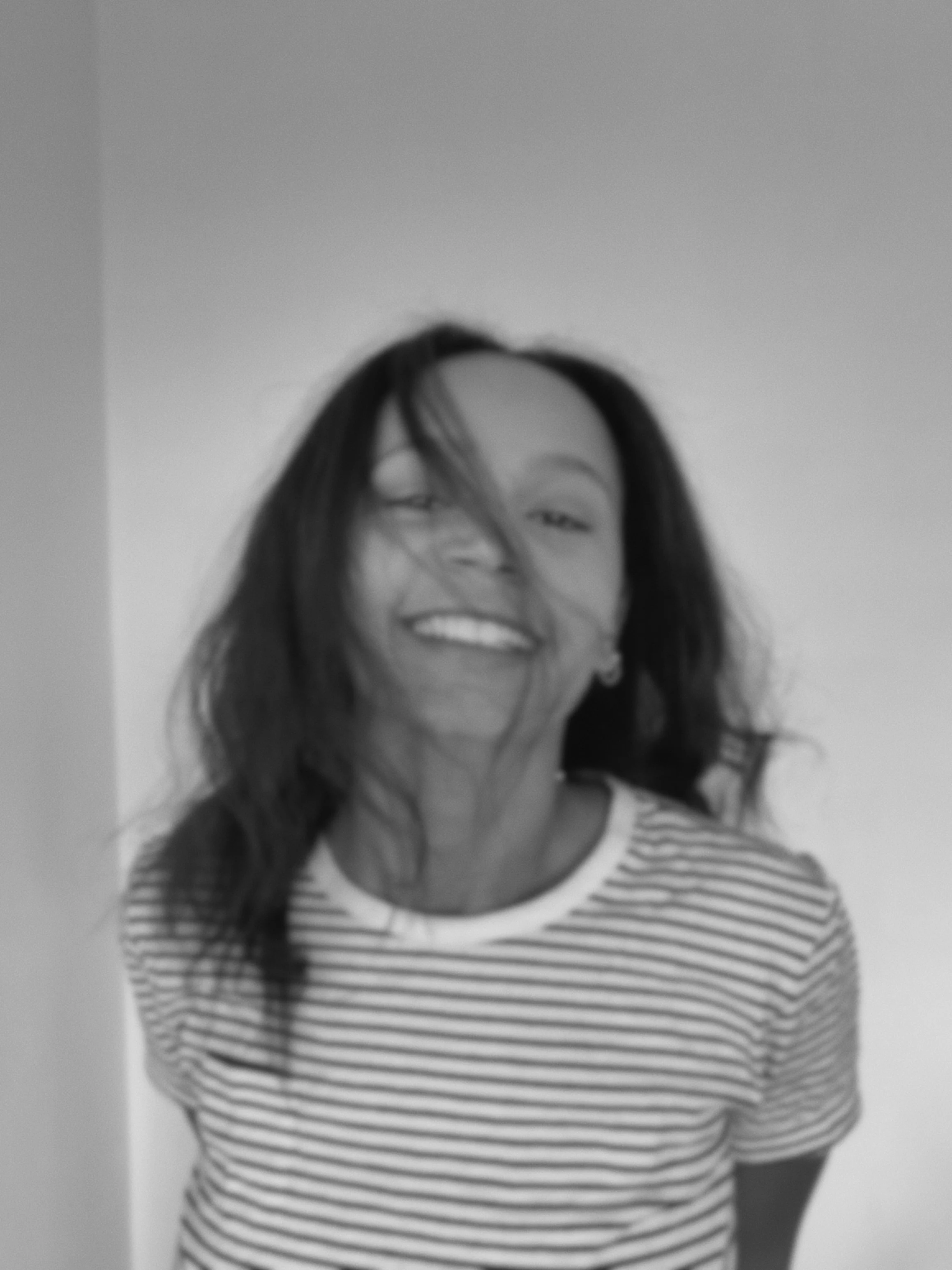 Jeune femme souriante avec des cheveux longs et foncés, portant un t-shirt à rayures, posant devant un mur clair.