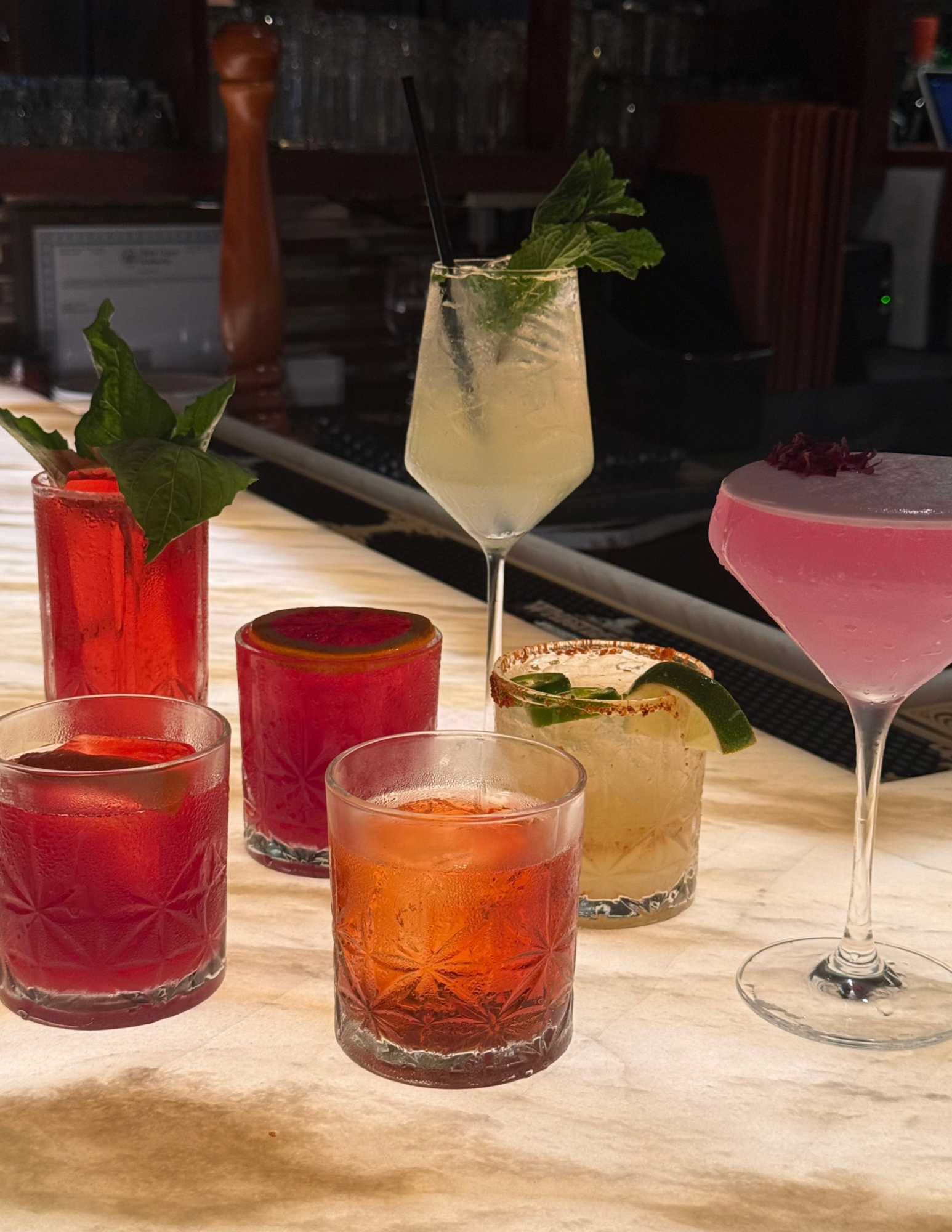 Collection of colorful cocktails on a bar counter, featuring various glasses with garnishes and vibrant drinks.