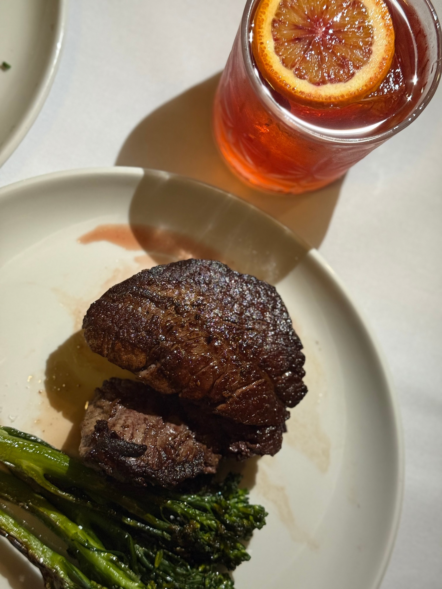 A plate with a cooked steak, grilled asparagus, and some sauce, accompanied by a glass of iced tea with lemon slices.