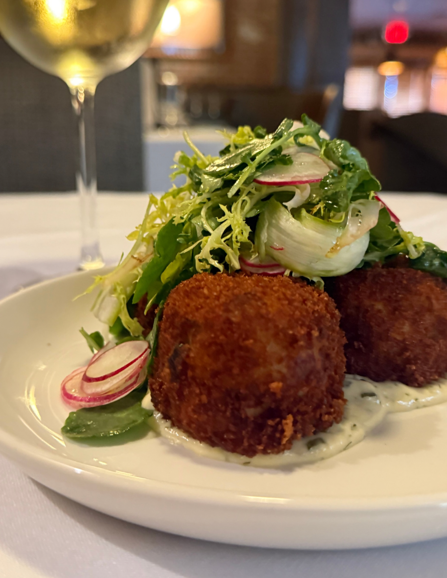 Fried croquettes served with salad and radish slices on a white plate at a restaurant.