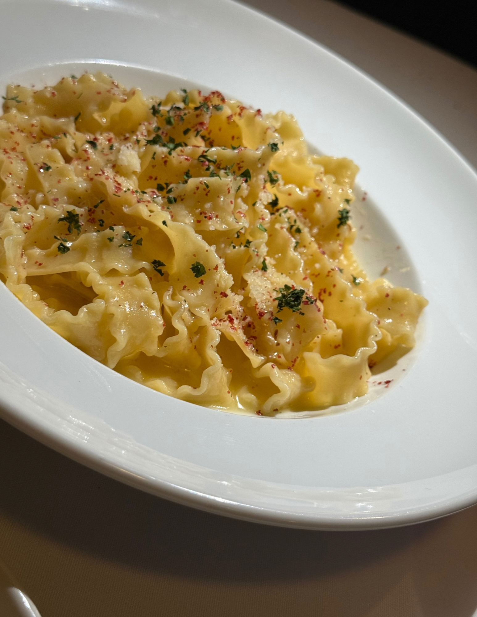 Close-up of cooked Italy-style pasta with parsley and red pepper flakes in a white bowl.