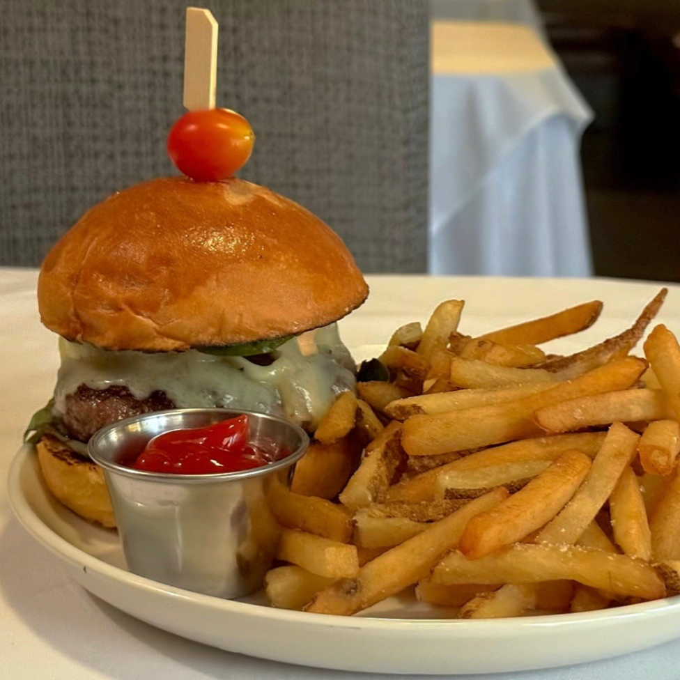 A plate with a cheeseburger topped with a cherry tomato and a skewer, serving of French fries with ketchup.