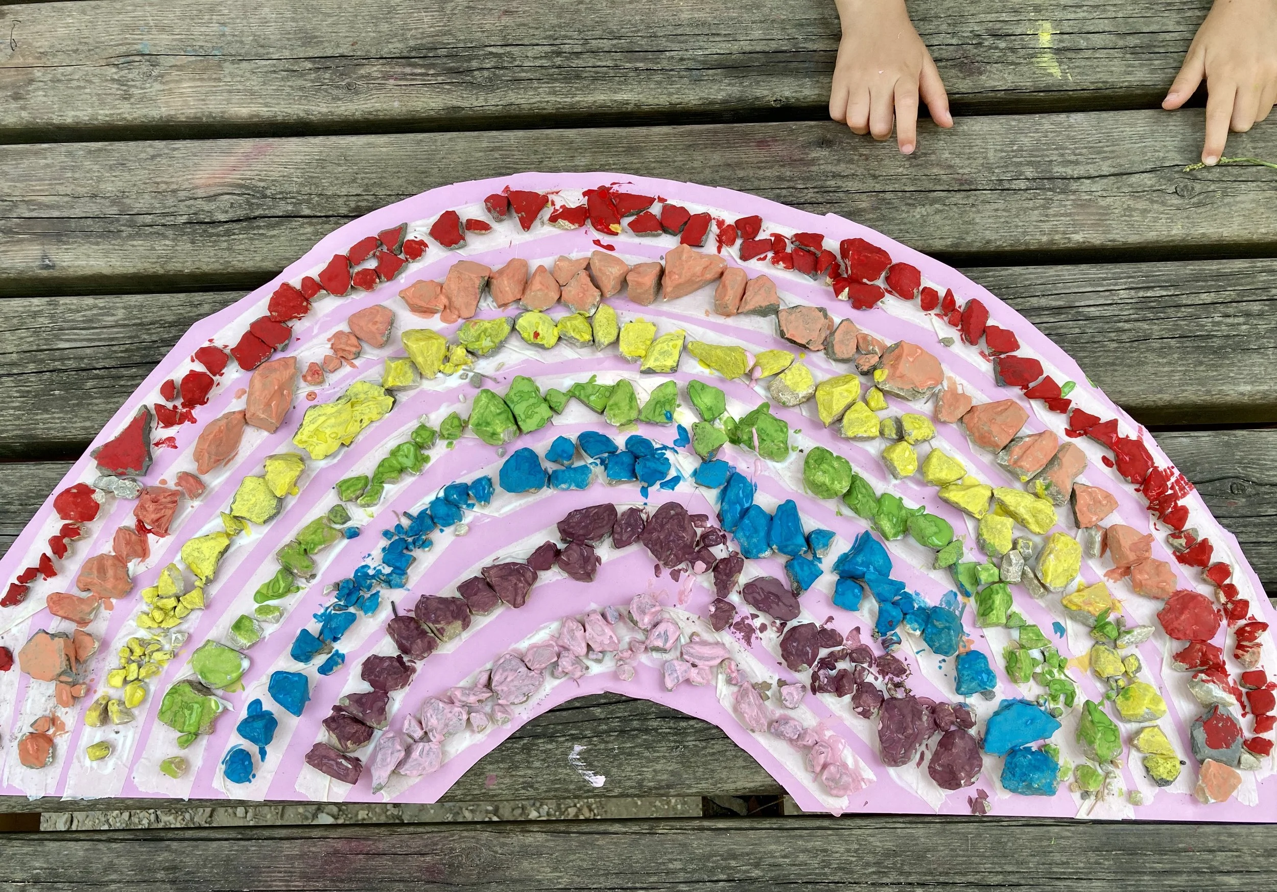 Una tavola di legno con un grande arco di pietre colorate di vari colori, probabilmente un arcobaleno di pietre o mosaico fatto a mano.