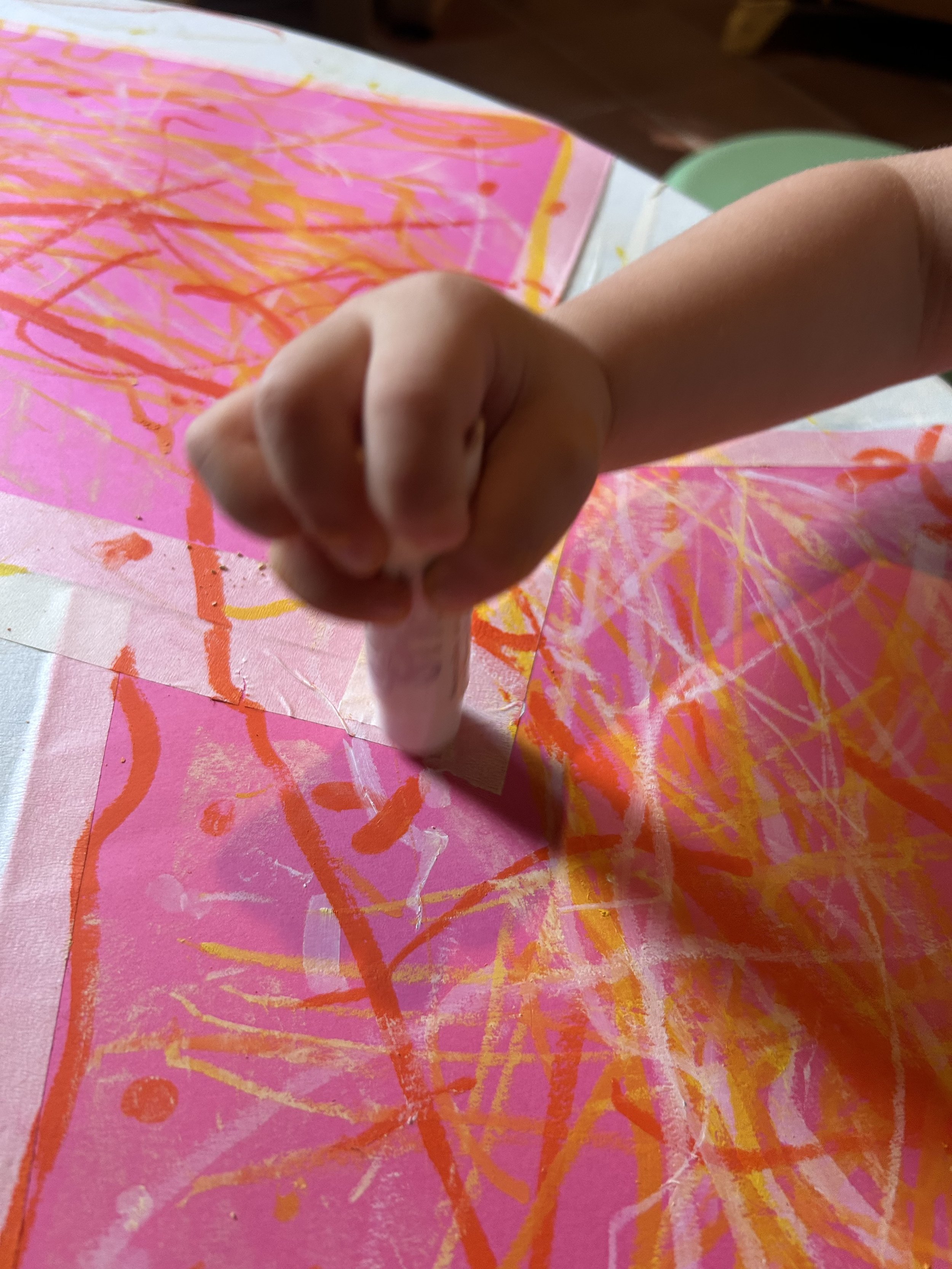 Un bambino sta creando un dipinto con colori vivaci su carta rosa, usando un pennello o uno strumento simile.