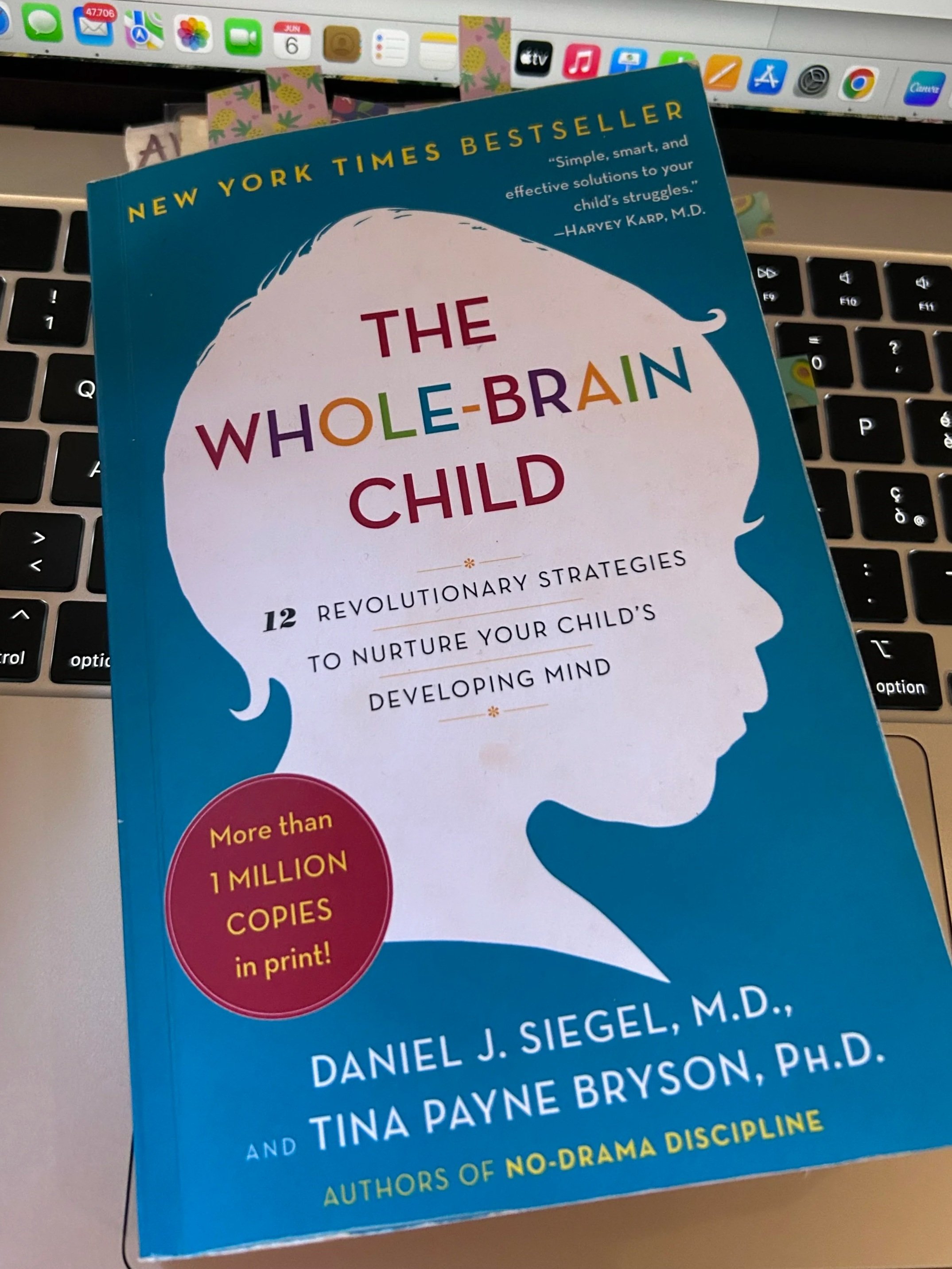 Copertina di un libro intitolato "The Whole-Brain Child" di Daniel J. Siegel e Tina Payne Bryson, con uno sfondo blu e una sagoma di testa umana, posizionato sopra una tastiera di computer.