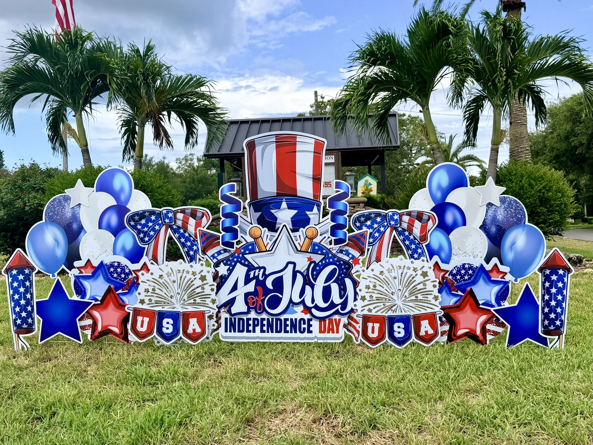 Patriotic Fourth of July or Independence Day display with balloons, stars, and banners in red, white, and blue, featuring a large sign that reads 'Happy 4th of July' and 'USA'.