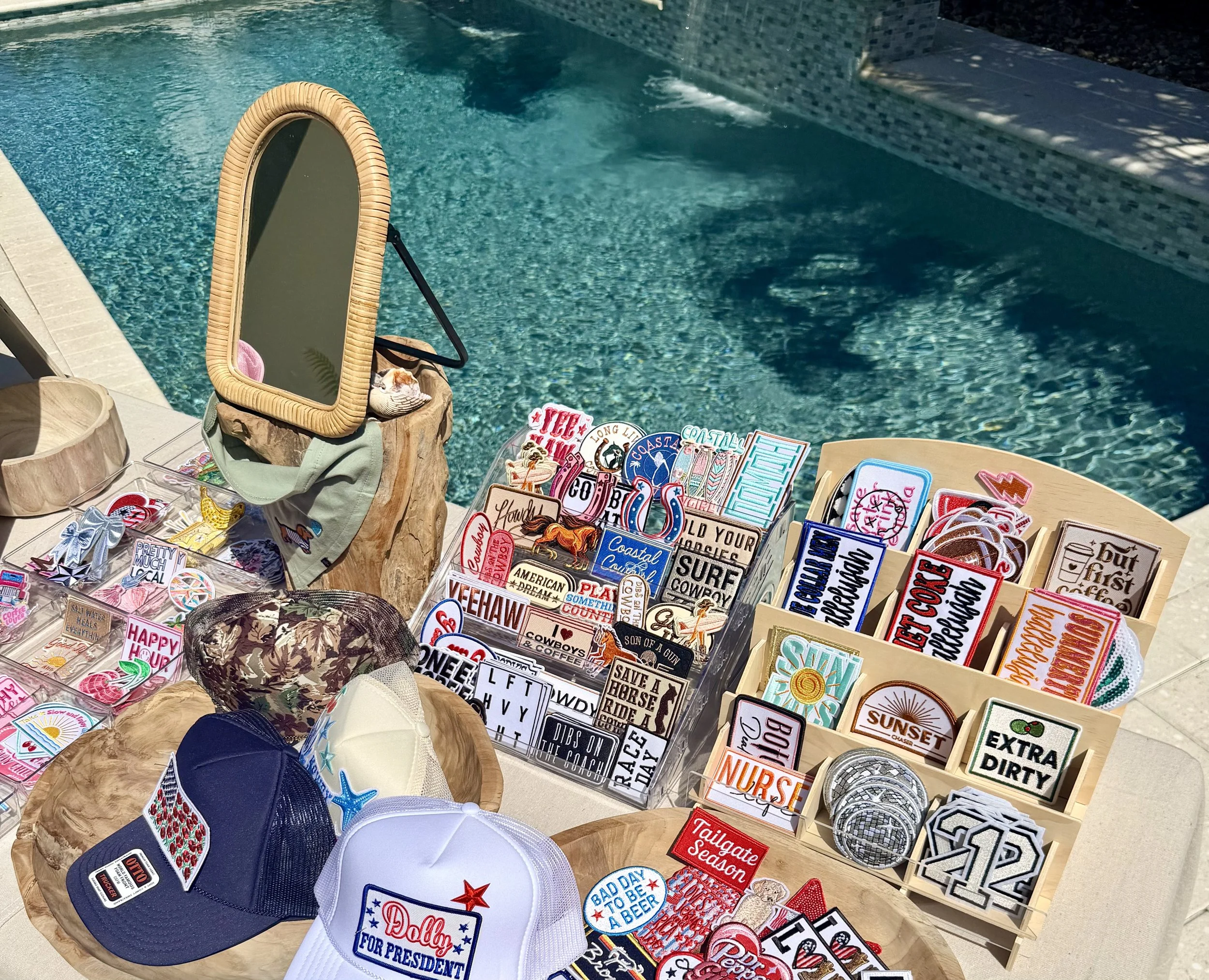 Display of various patriotic and humorous patches and patches, hats with American flags, with a swimming pool in the background.