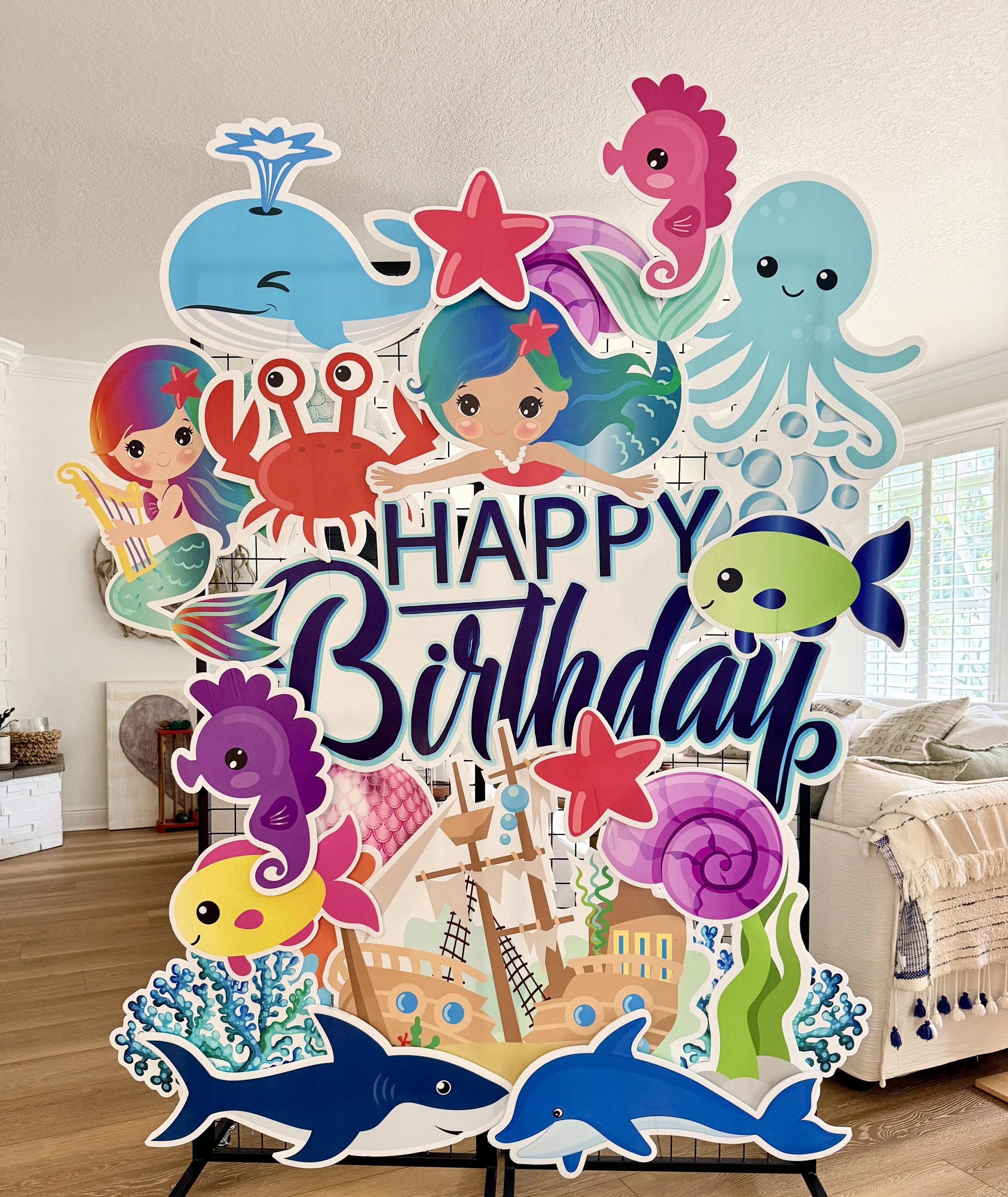 Colorful, cartoon-style ocean-themed birthday sign featuring a whale, octopus, seahorse, crab, mermaid, fish, stingray, and coral, with the text 'Happy Birthday' in the center.