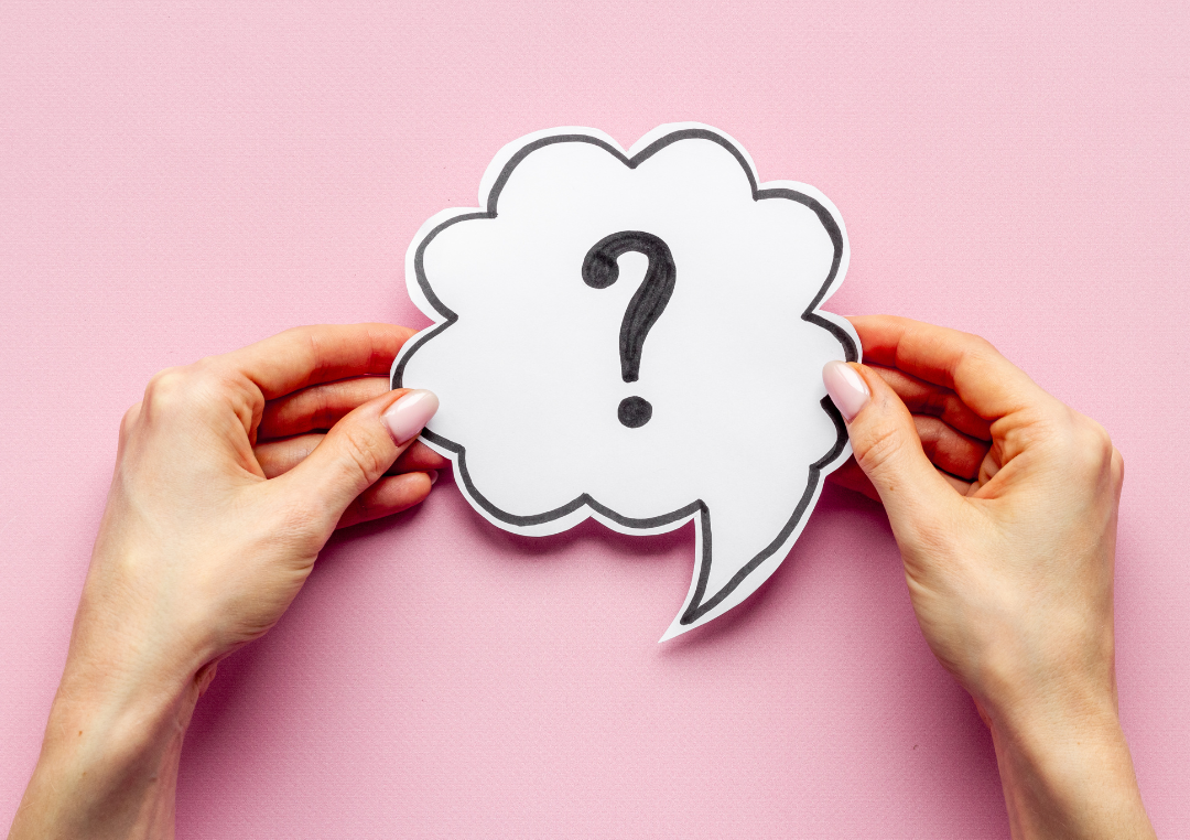 Hands holding a paper speech bubble with a question mark on a pink background.