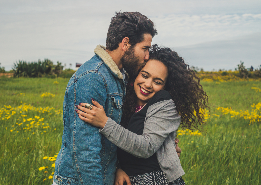 Couple sharing an affectionate moment in a field of yellow flowers.