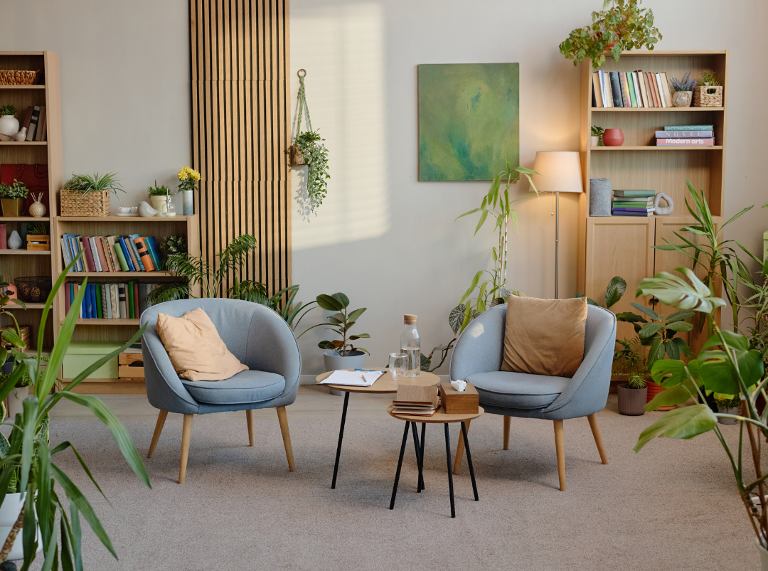 Warm counseling office with two armchairs, bookshelves, plants, and soft lighting.