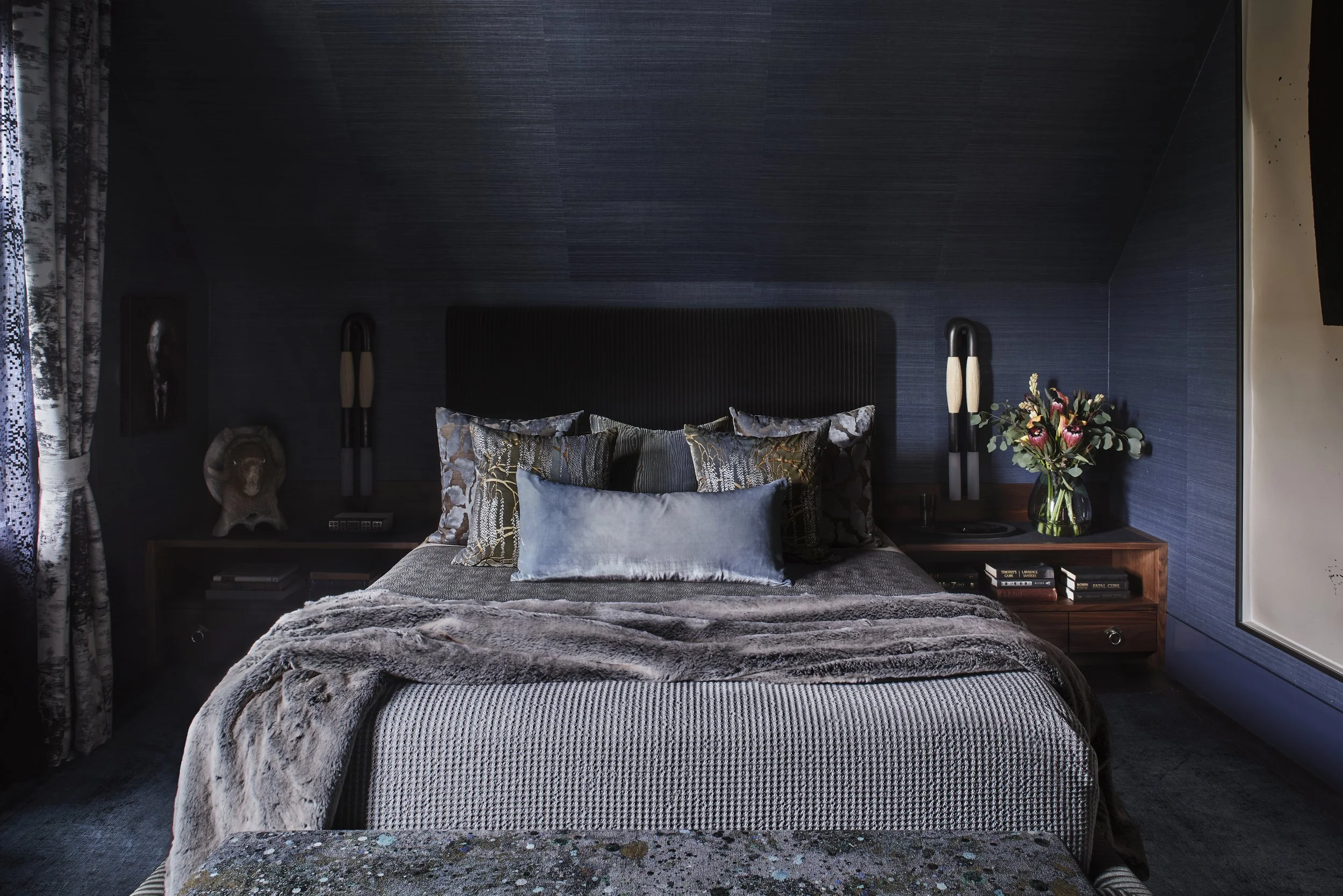 Bedroom featuring dark blue textured walls, a bed with an upholstered dark blue headboard, a gray textured duvet, and wooden side tables.