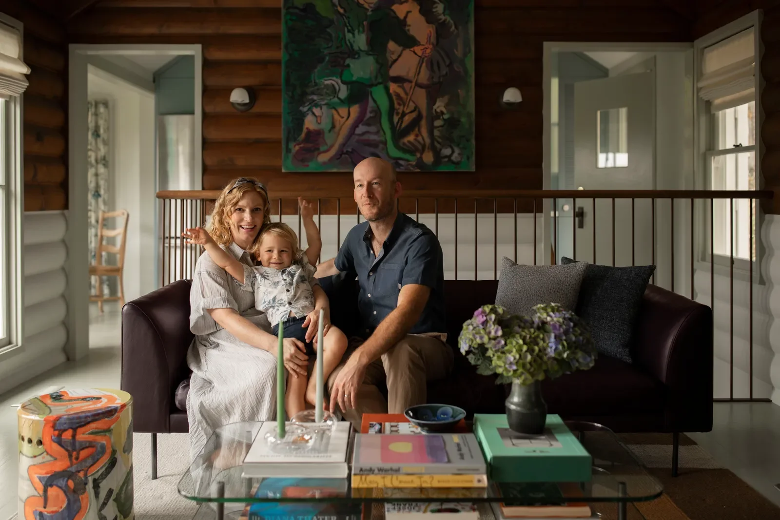 Family portrait featuring architect Benjamin McGriff, his wife Julia, and their daughter Nancy seated together on a dark leather sofa in a wood-paneled living room, surrounded by modern art books and contemporary decor.