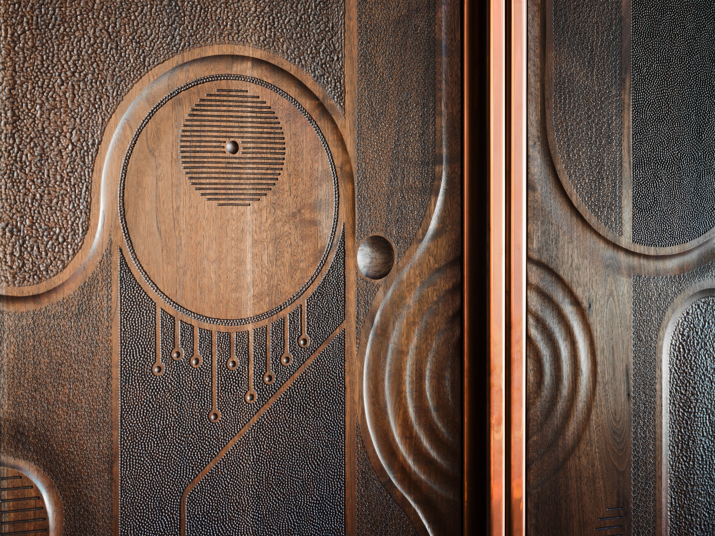 Close-up of custom wood-carved cabinet doors featuring an intricate circular geometric design and fine metal detailing.
