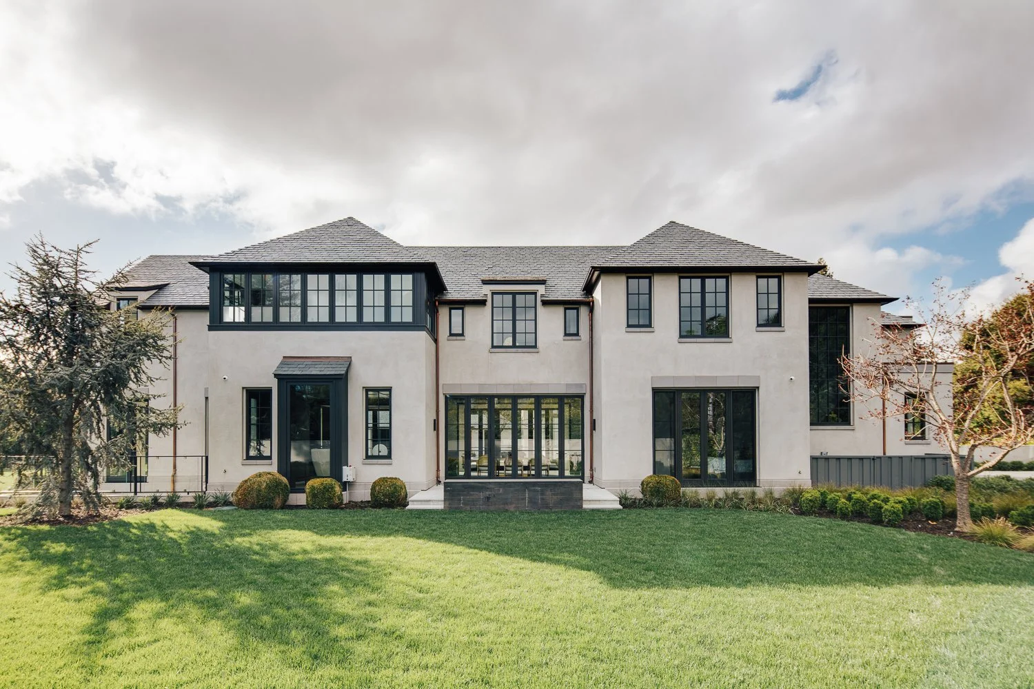 An exterior facade view of the home featuring windows of various sizes and surrounding lawn areas.