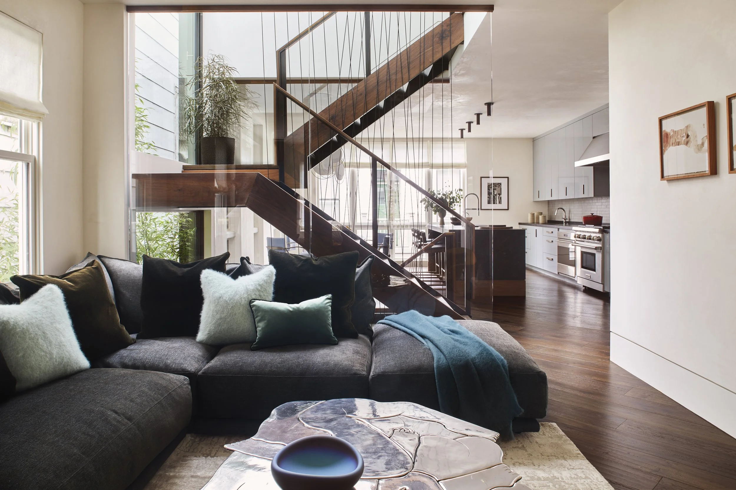 Interior view showing a multi-level staircase with glass partition walls separating the living room from an open plan kitchen and dining area. 