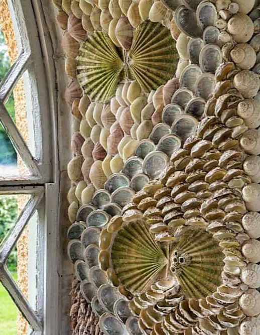 Close-up of ornate shellwork composed of overlapping seashells arranged in fan and floral patterns around a window.