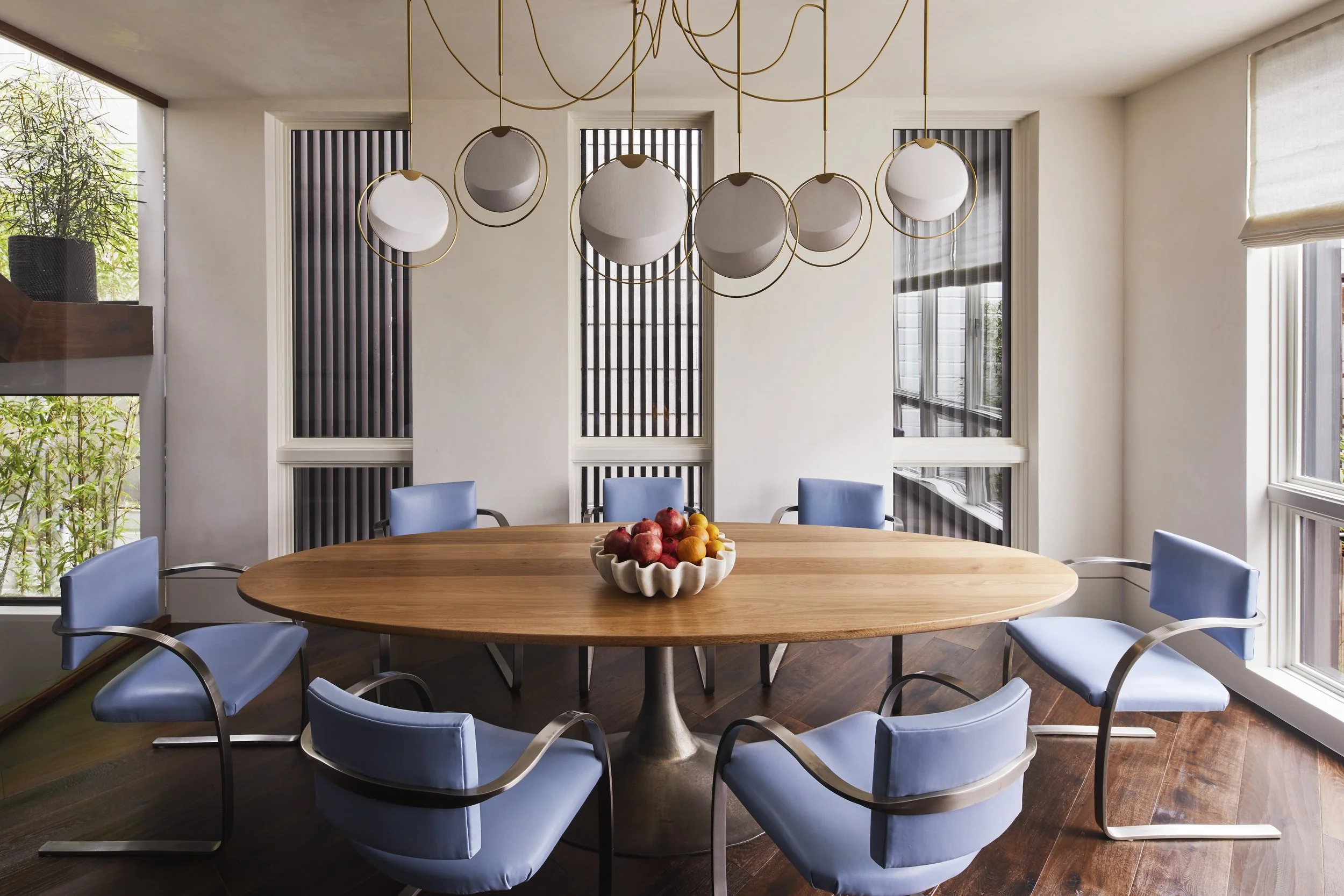 View of the dining area featuring a long oval wood dining table, light blue upholstered chairs, and a chandelier with multiple circular pendants.