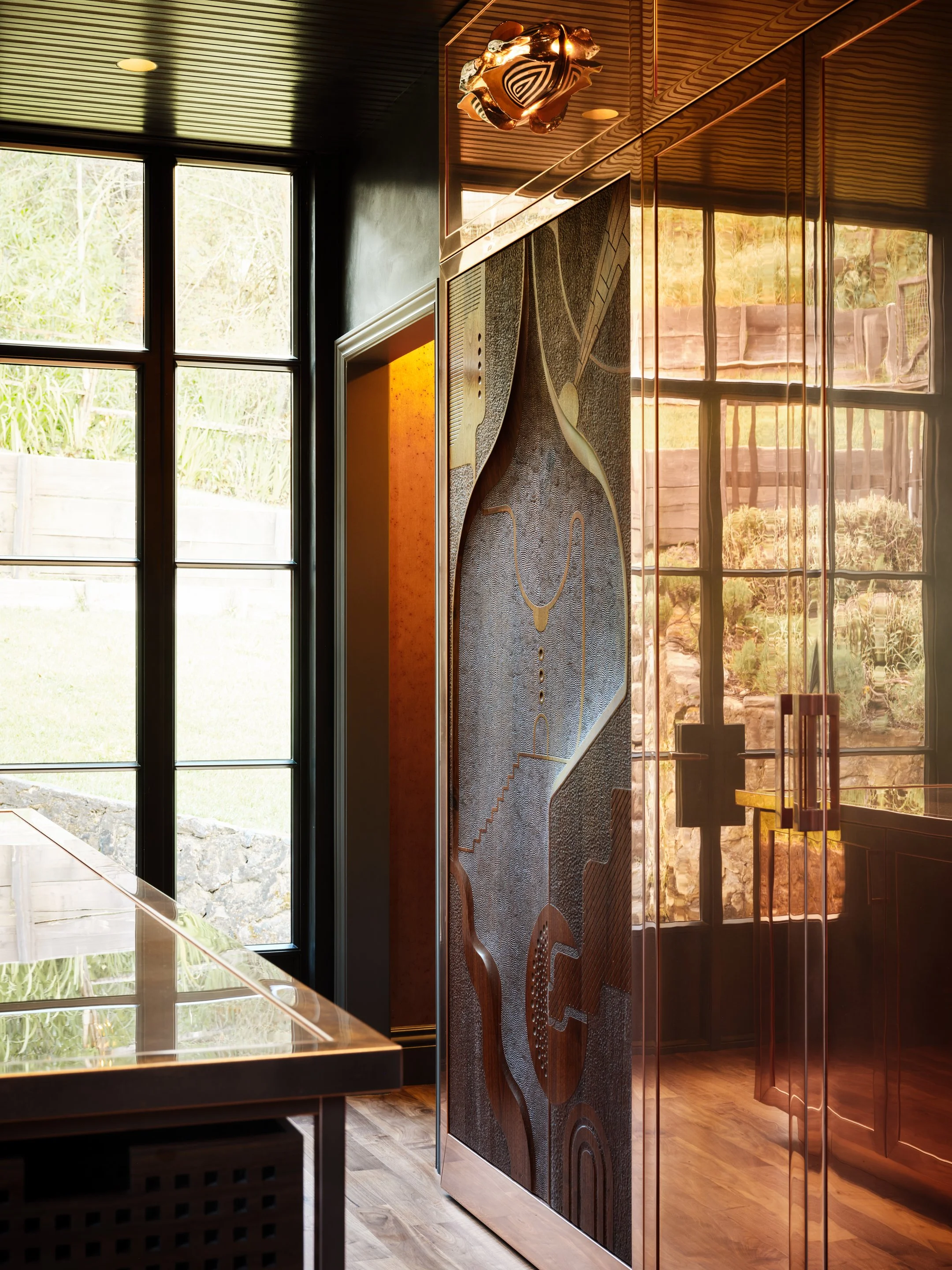 View of kitchen cabinetry in a combination of intricate carved designs and clean copper, with natural light coming through floor-to-ceiling windows.