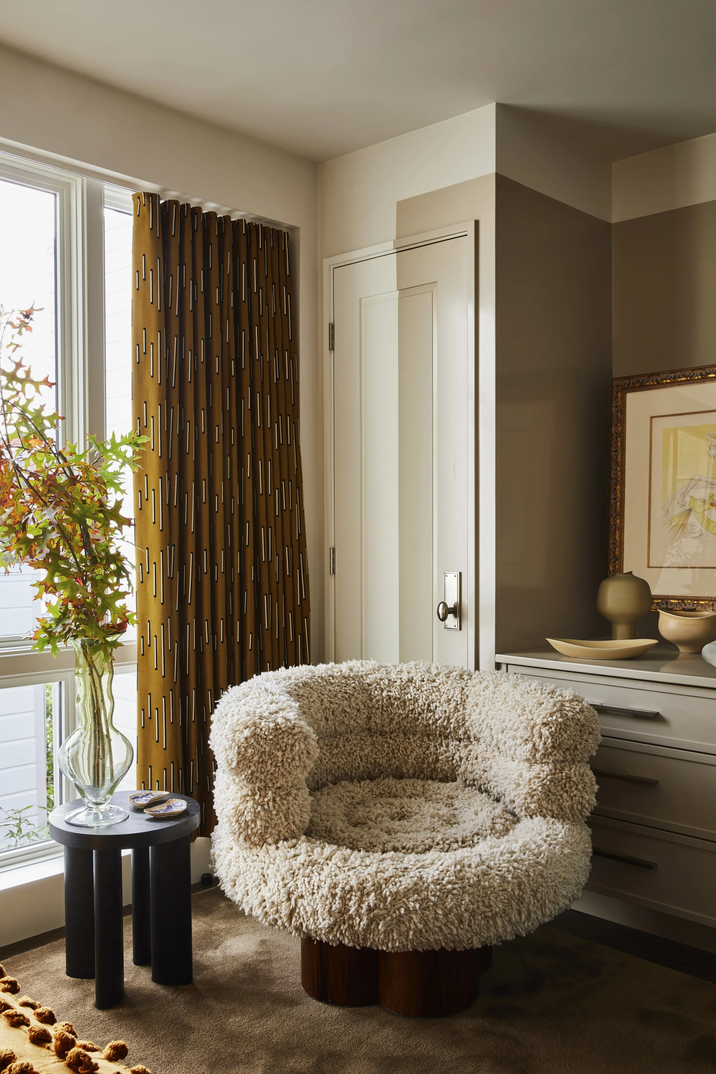 Bedroom sitting area featuring a large window with patterned drapes and a thickly textured round armchair.