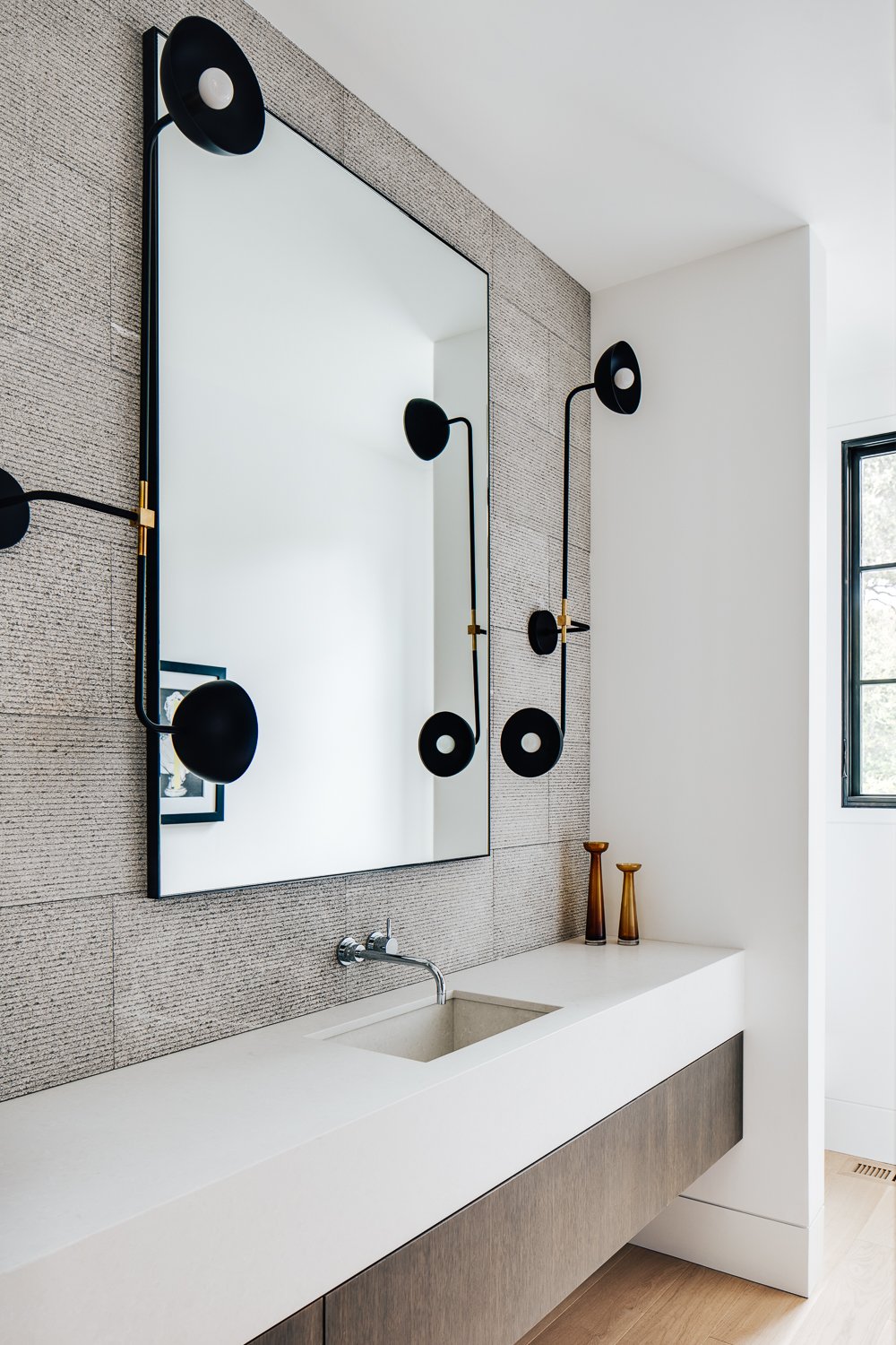 Clean, bright vanity area featuring a sleek white countertop and sink and a large rectangular mirror on a textured wall, with dual wall sconces on either side.