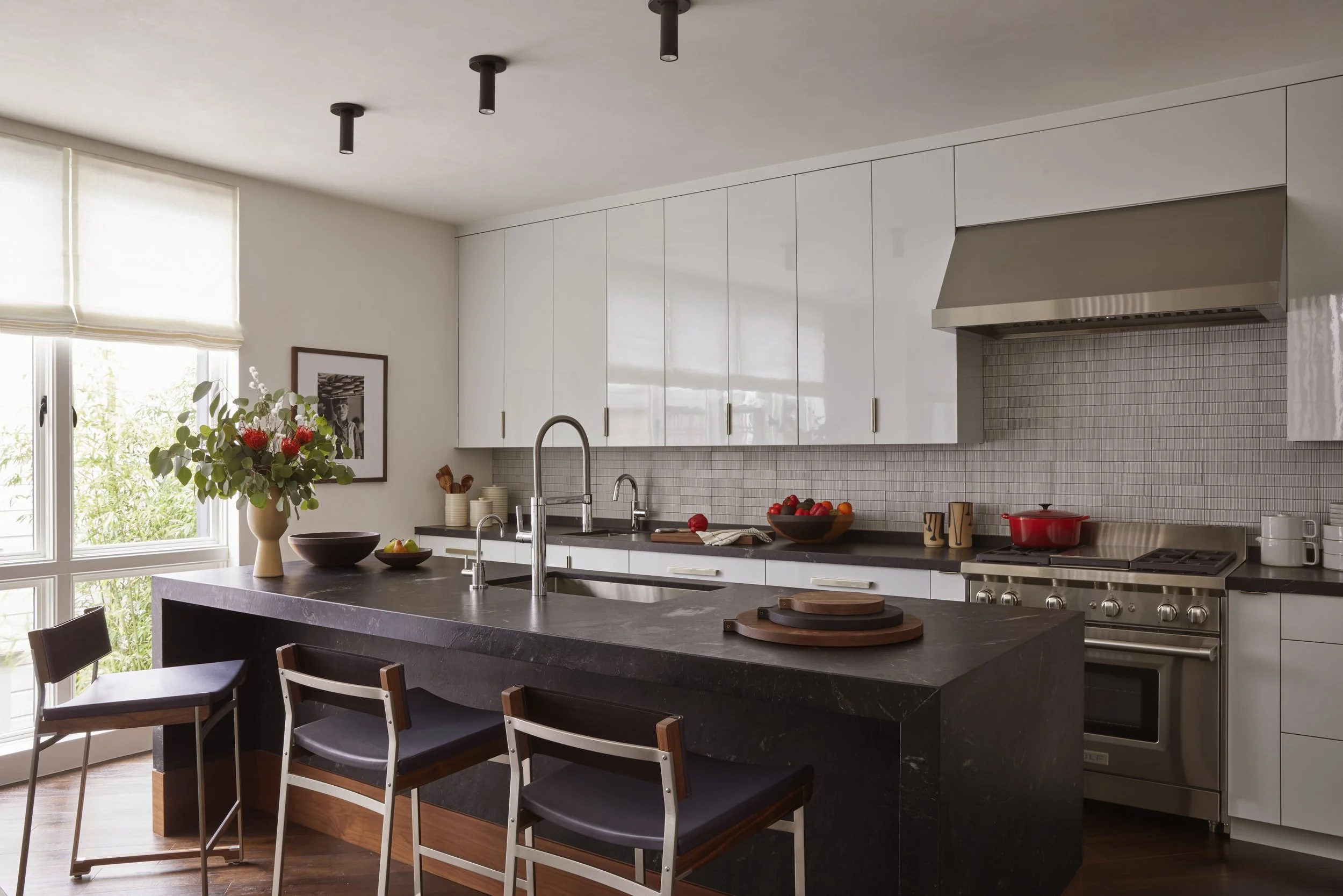 View of the kitchen with a dark stone island, three bar stools, and white cabinetry.