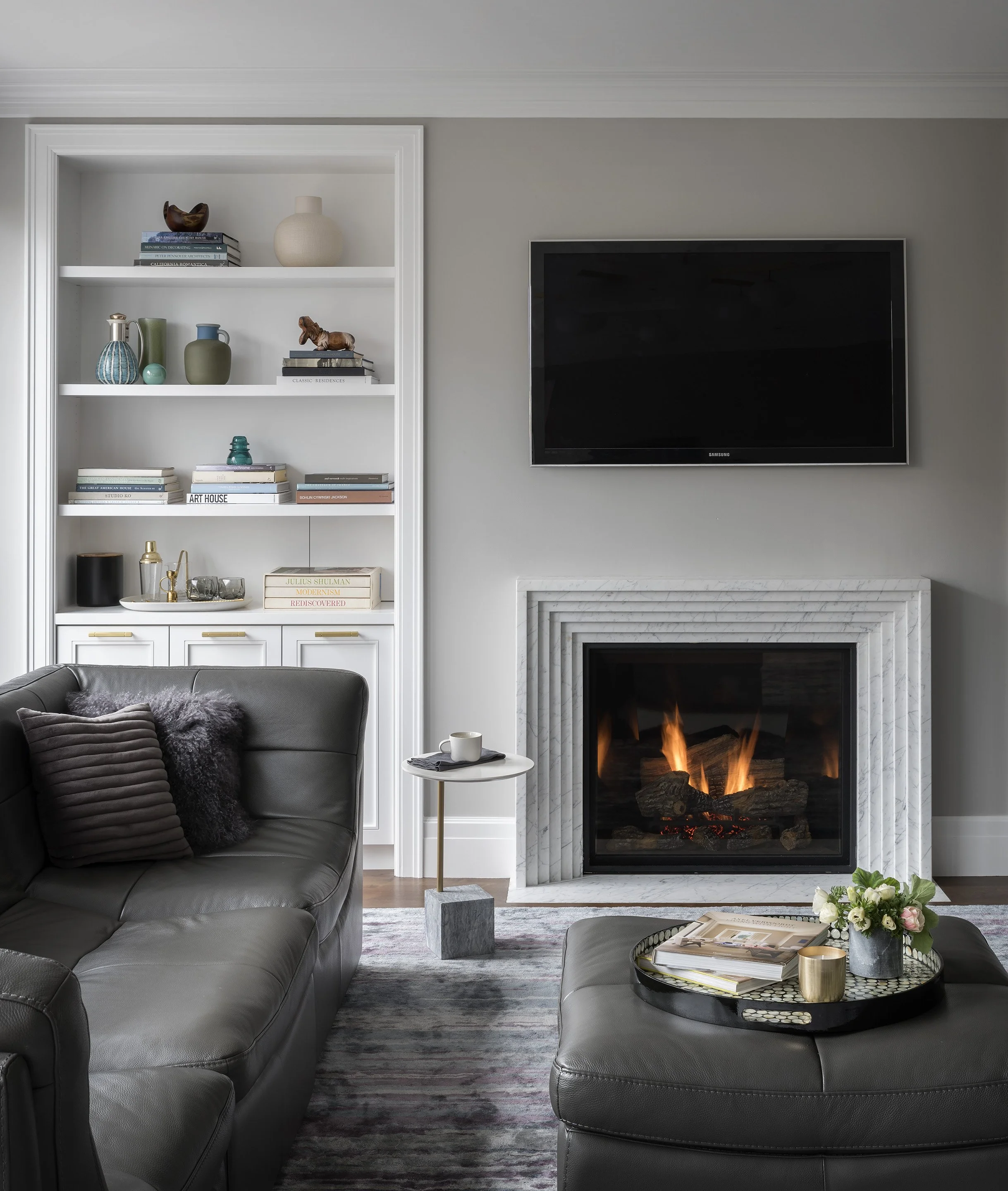 Interior view of a sitting room with a modern fireplace, built-in white shelving, a plush dark sofa and matching ottoman.