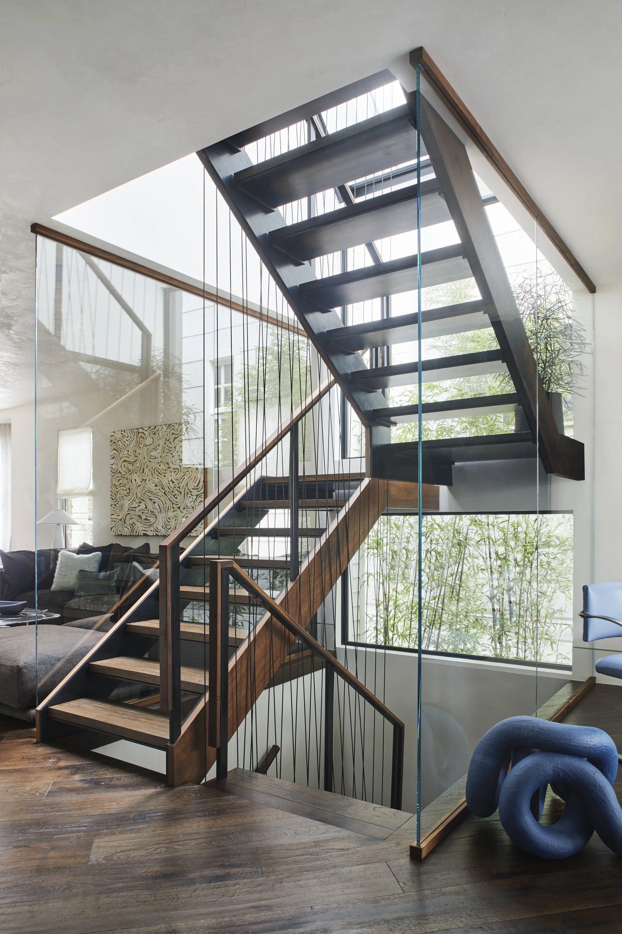 Close-up of the interior stair landing featuring dark metal structural railings, glass partition walls, and a sightline overlooking the lower level.