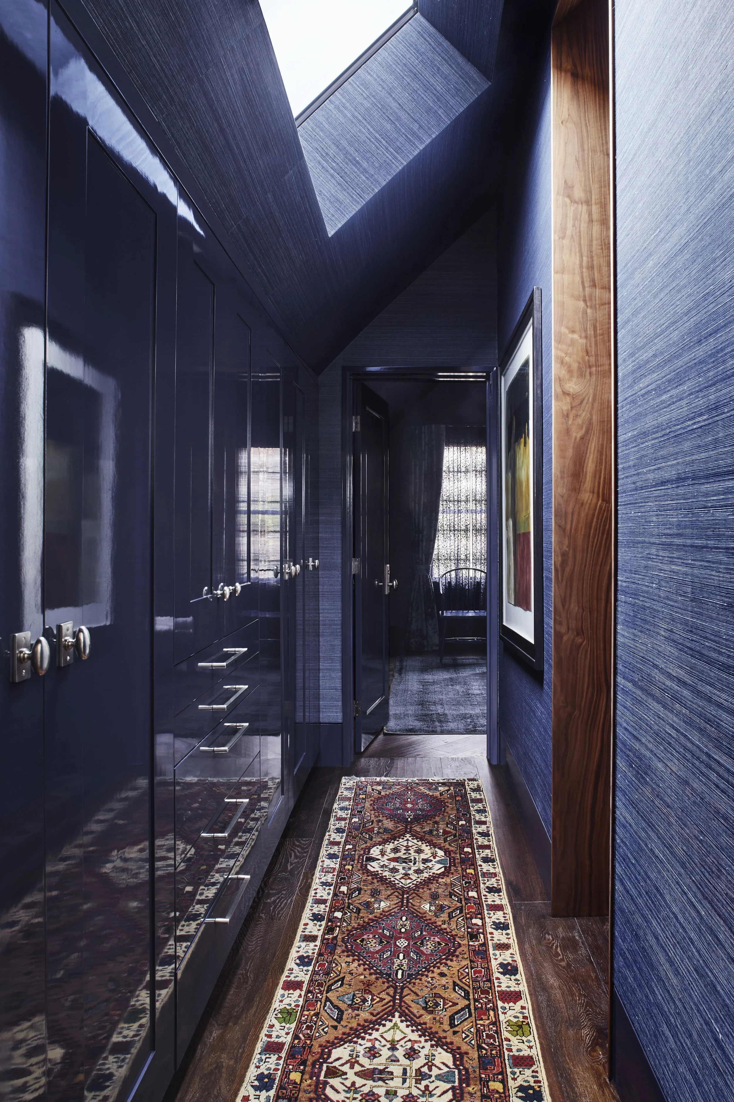A hallway view with dark blue textured walls and a wall of floor-to-ceiling built-in cabinets painted in a dark blue lacquer finish. 