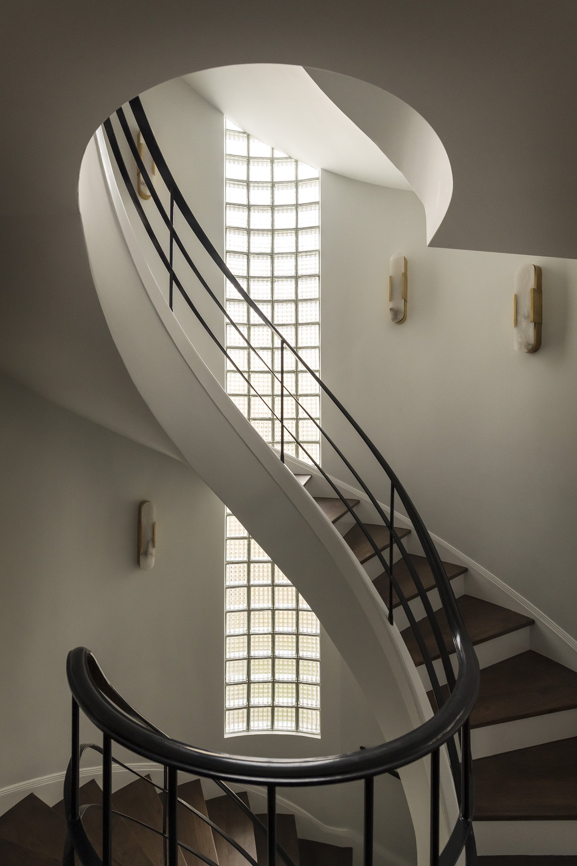 Architectural staircase featuring a dramatic curved white stairwell with dark metal railings and a long vertical glass-block window.