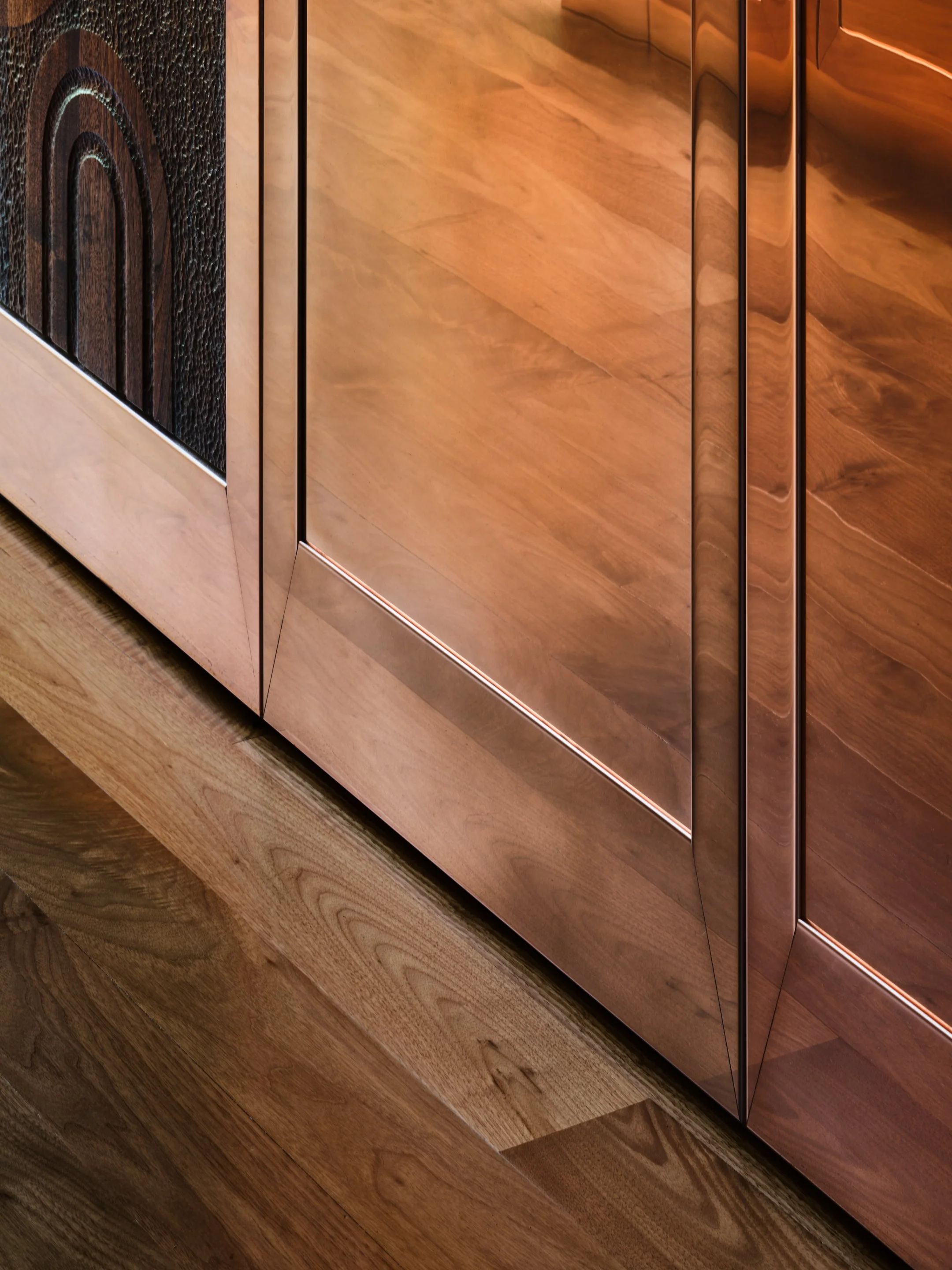 Close-up of copper cabinet front, with hardwood floors underneath.