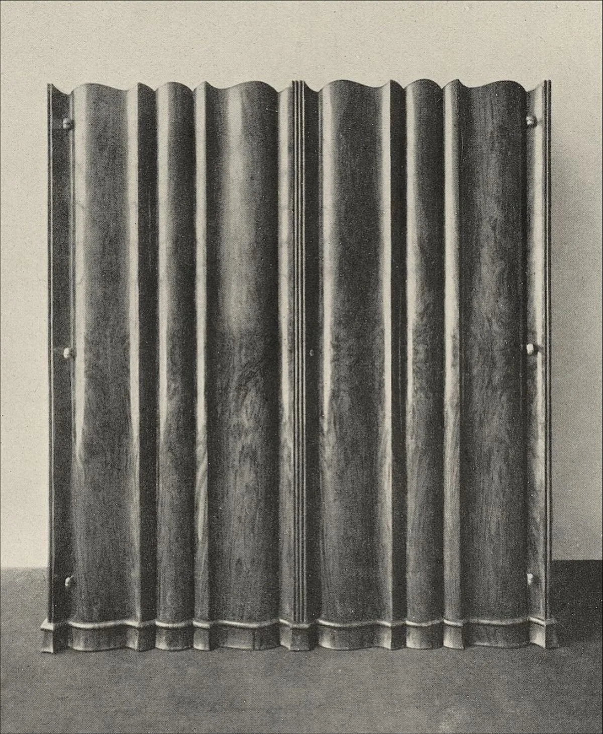 Black-and-white photograph of a sculptural wood screen composed of repeating vertical, undulating panels.