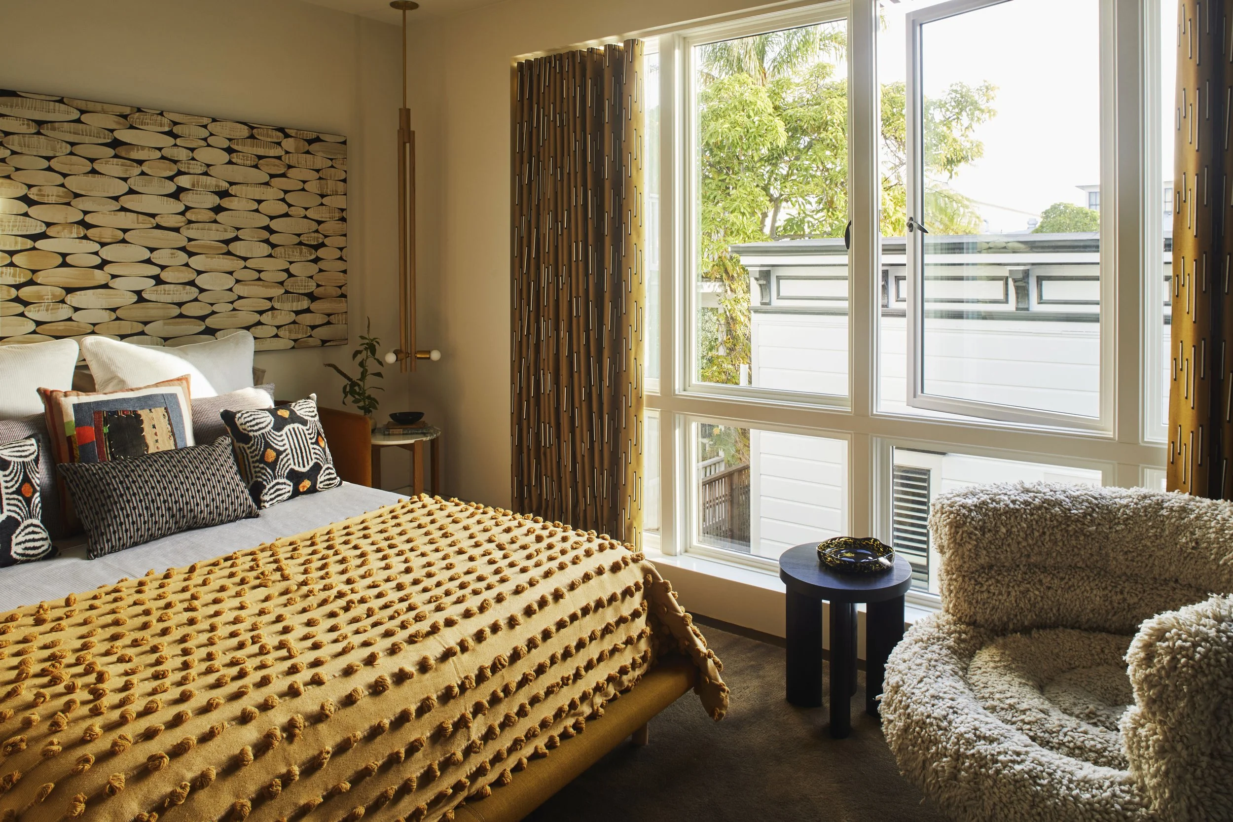 Bedroom view featuring large floor-to-ceiling windows, a bed with a textured yellow duvet, and a cozy round armchair.