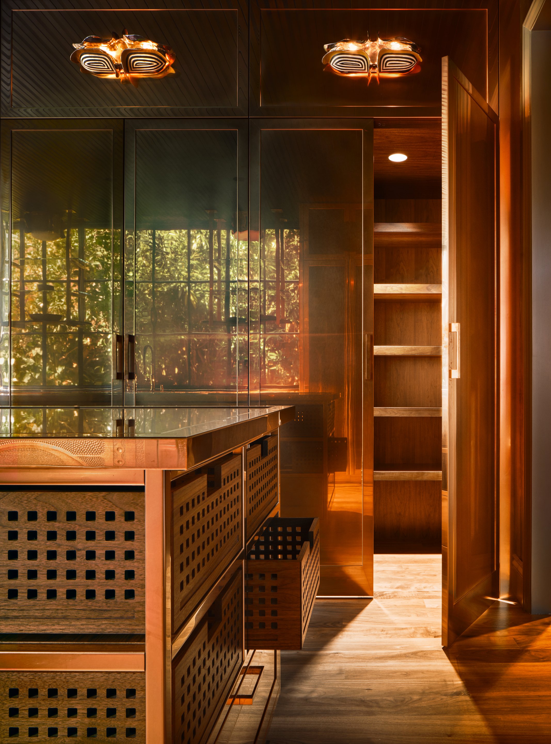 View through an open copper door to floor-to-ceiling cabinet interior with wooden shelves under warm lighting.