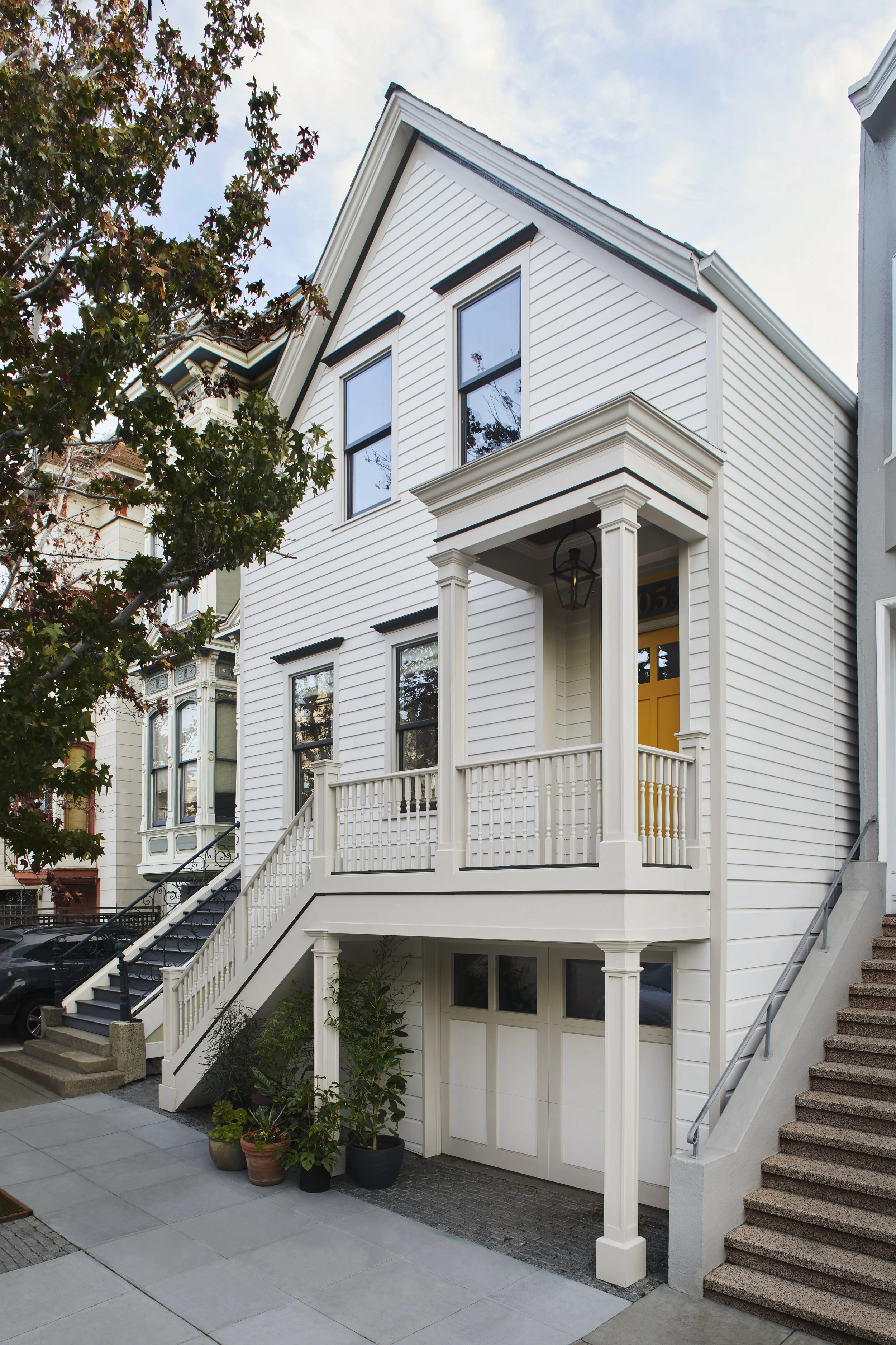 Exterior front view of a white multi-level home with a covered entryway, stairs, and vertical windows.