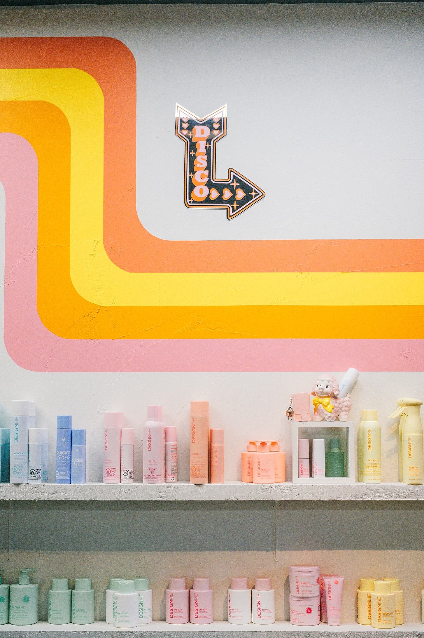 Store shelf displaying pastel-colored bottles of hair or skincare products arranged by color, with brands and labels partially visible.