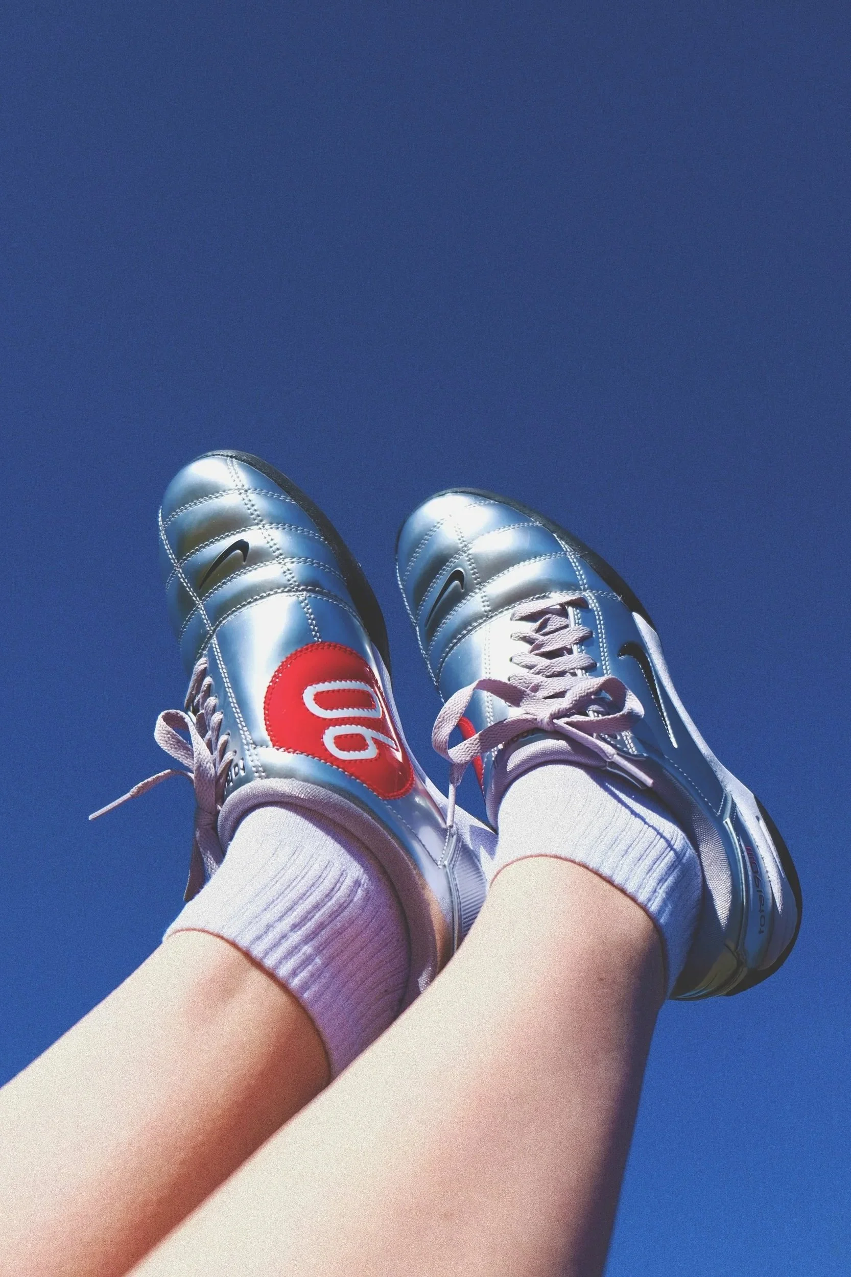 Two people with shiny silver athletic shoes, white socks with red accents, and white athletic shorts, are skydiving.