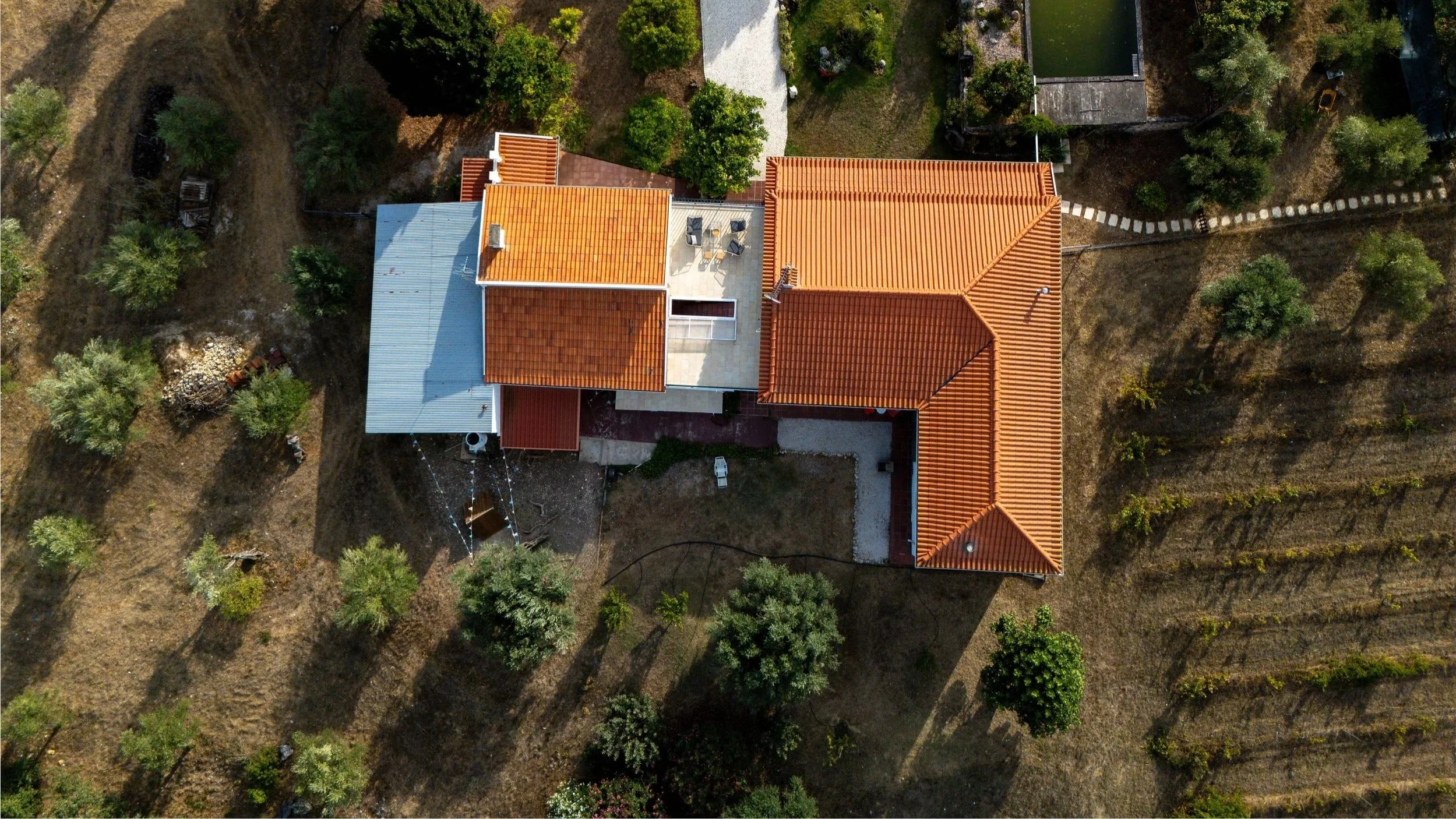 A bird's-eye view of a quinta with a terracotta-colored roof, surrounded by gardens and olive trees.