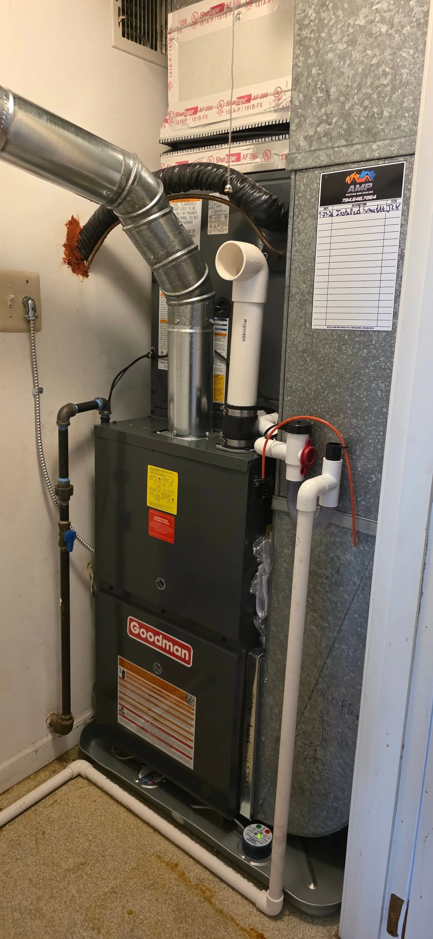 A Goodman furnace installed in a utility closet with ductwork and vent pipes, some of which are wrapped with black insulation; a water softener or filter system on the right side; and a label on the right wall reading 'Installed 7/22/14'.