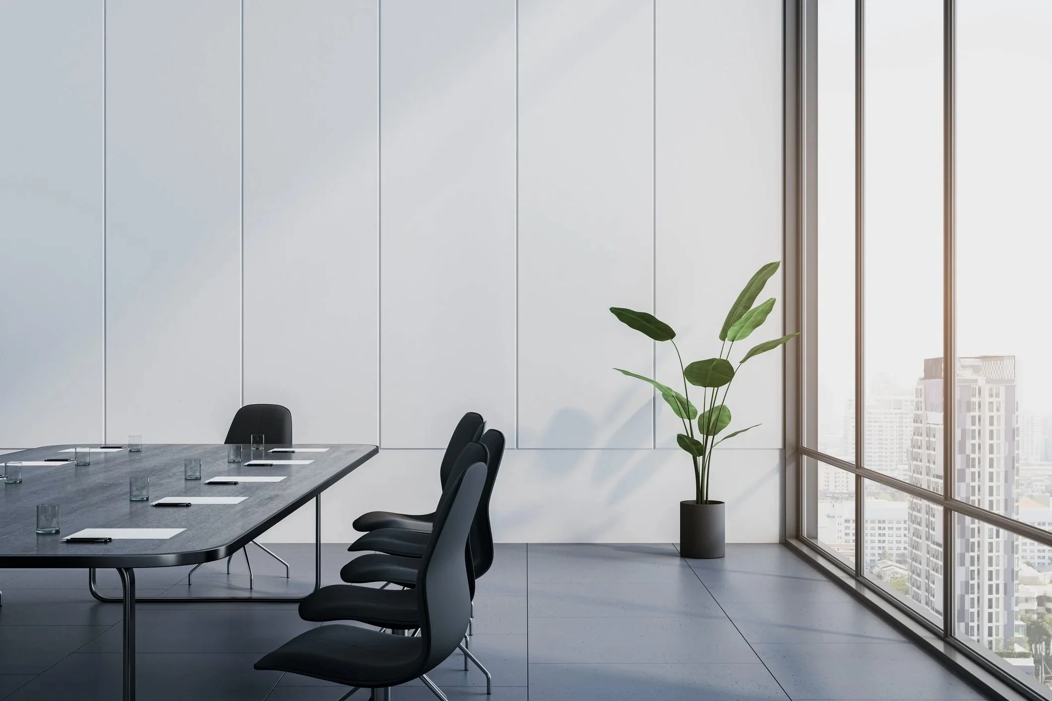 Modern conference room with a large table, black chairs, a potted plant, and floor-to-ceiling windows showing a cityscape.