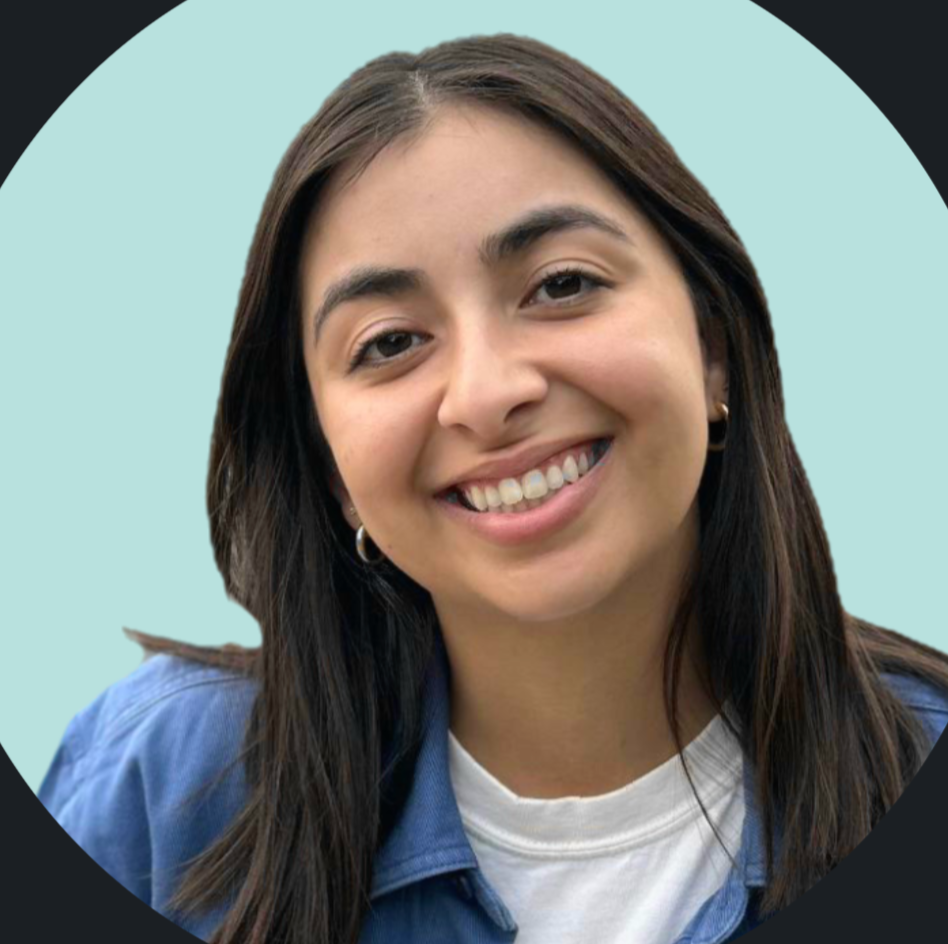 Young woman with long dark hair smiling, wearing a blue jacket with a white t-shirt underneath, in front of a light blue background